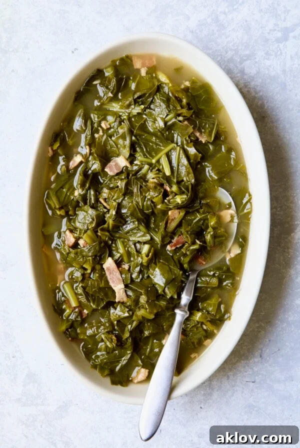 Braised Southern Greens in oval serving bowl with serving spoon on light blue background.