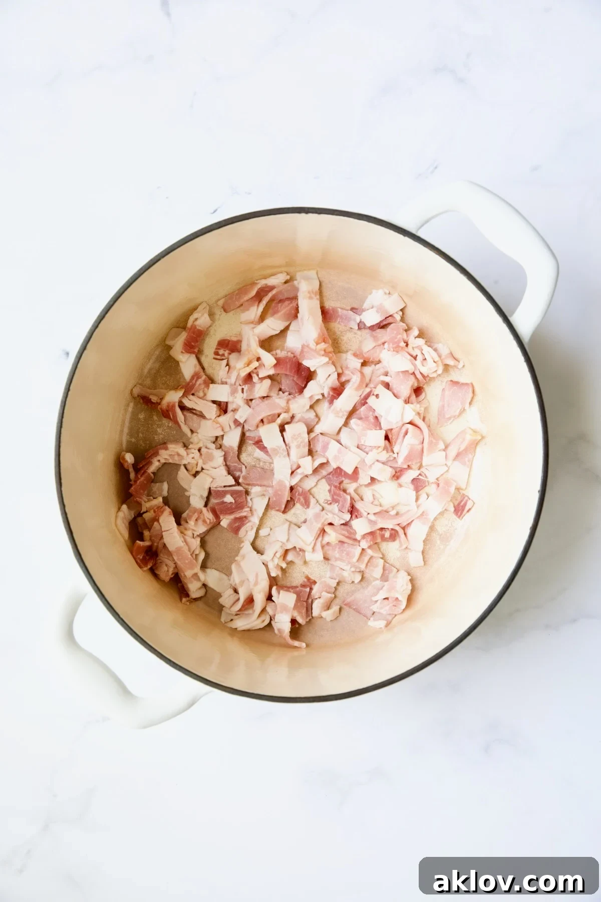Uncooked bacon in white Dutch oven.