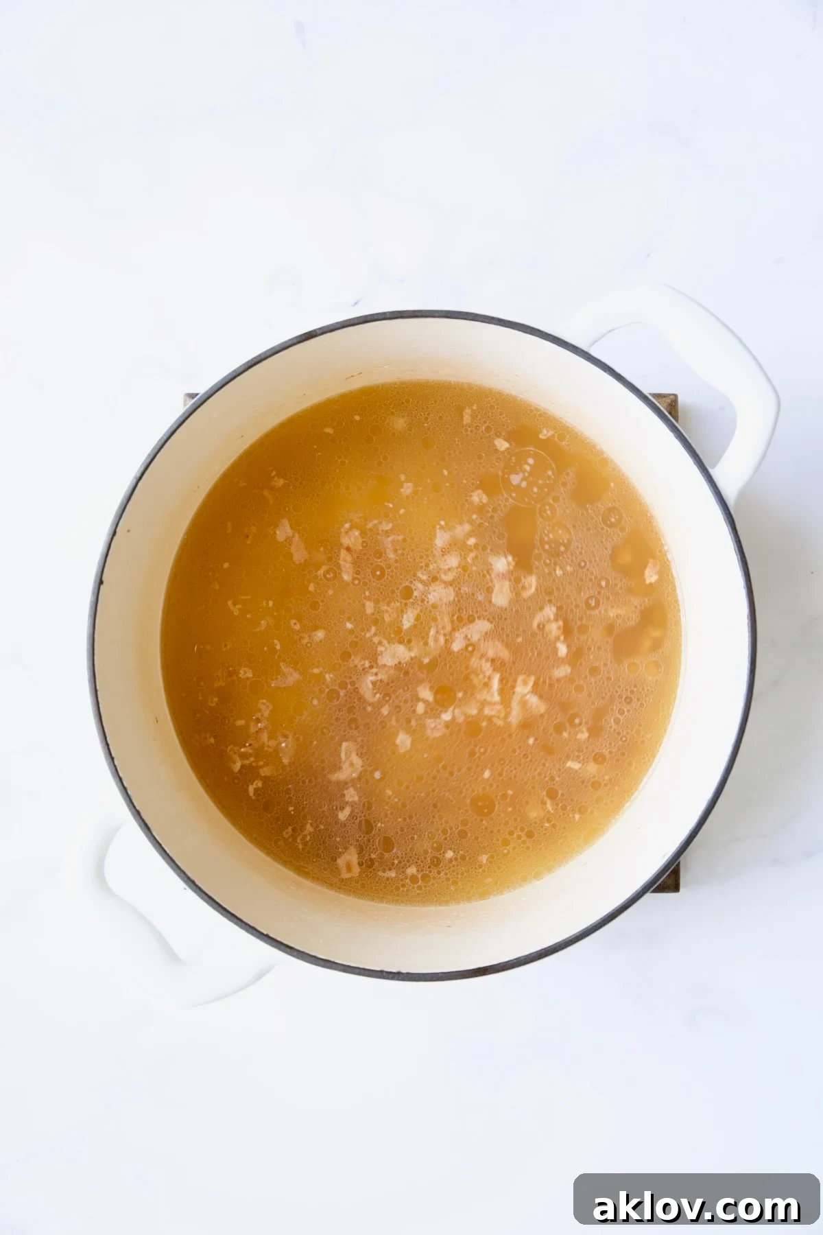 Chicken broth and bacon in white Dutch oven.