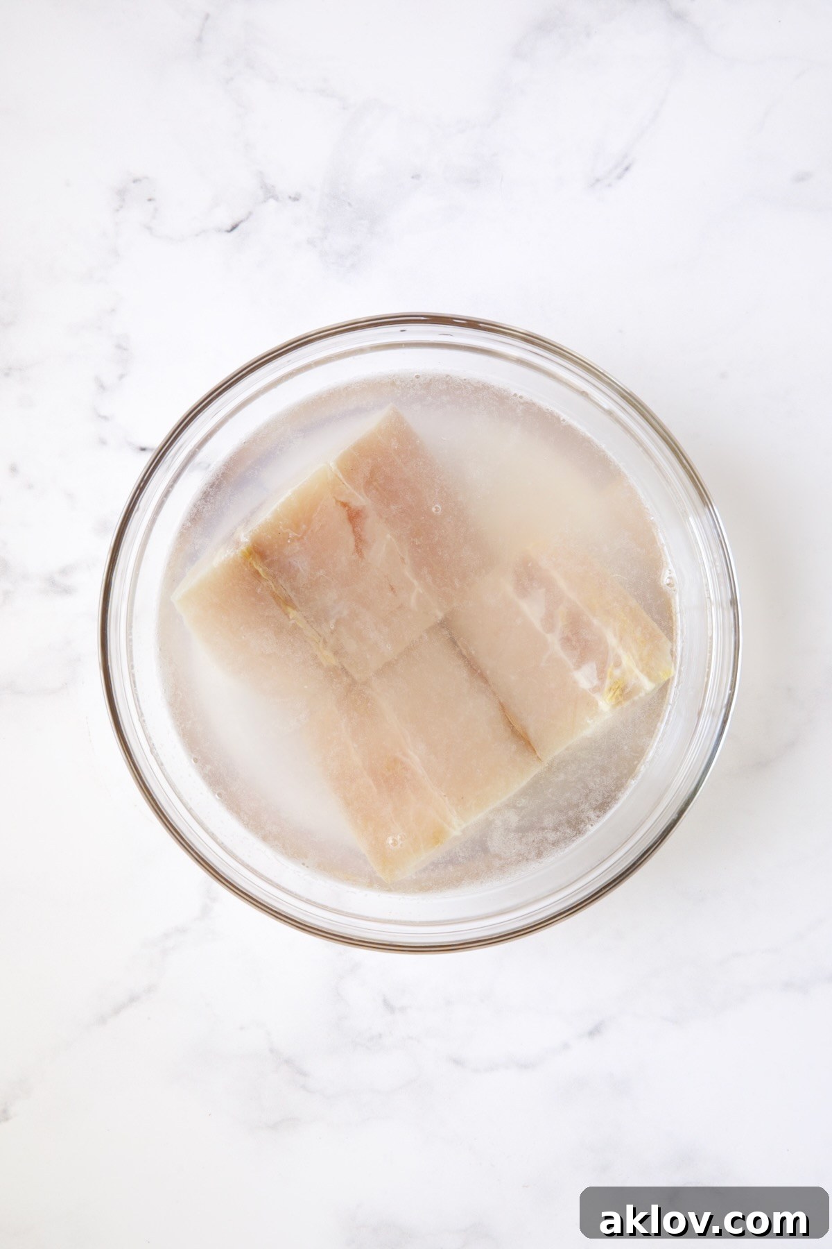 Two pieces of mahi-mahi fillets soaking in a simple brine of water and lime juice in a clear glass bowl.