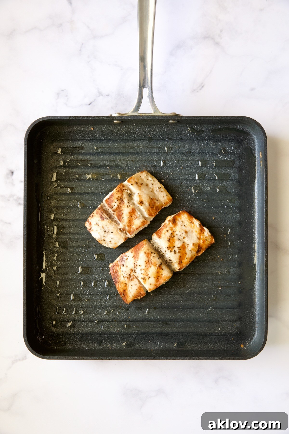 Two succulent pieces of grilled Mahi Mahi, showcasing beautiful grill marks, resting on a nonstick grill pan after being expertly cooked.