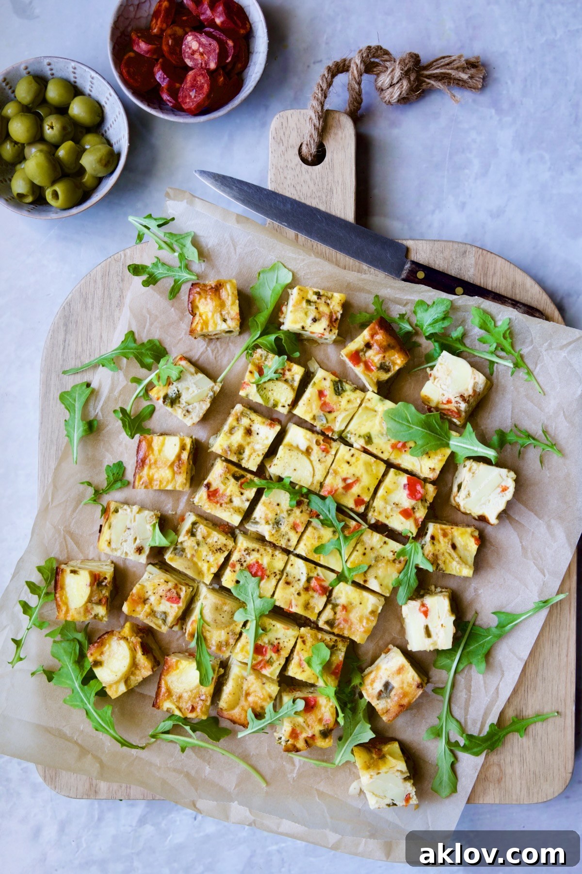 Oven-Baked Spanish Tortilla on parchment paper set on cutting board garnished with arugula.