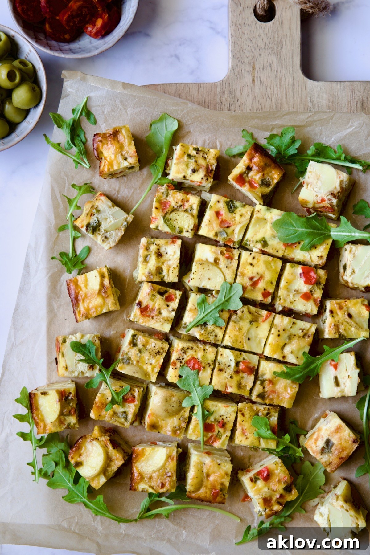 Oven-Baked Spanish Tortilla on parchment paper set on cutting board garnished with arugula.