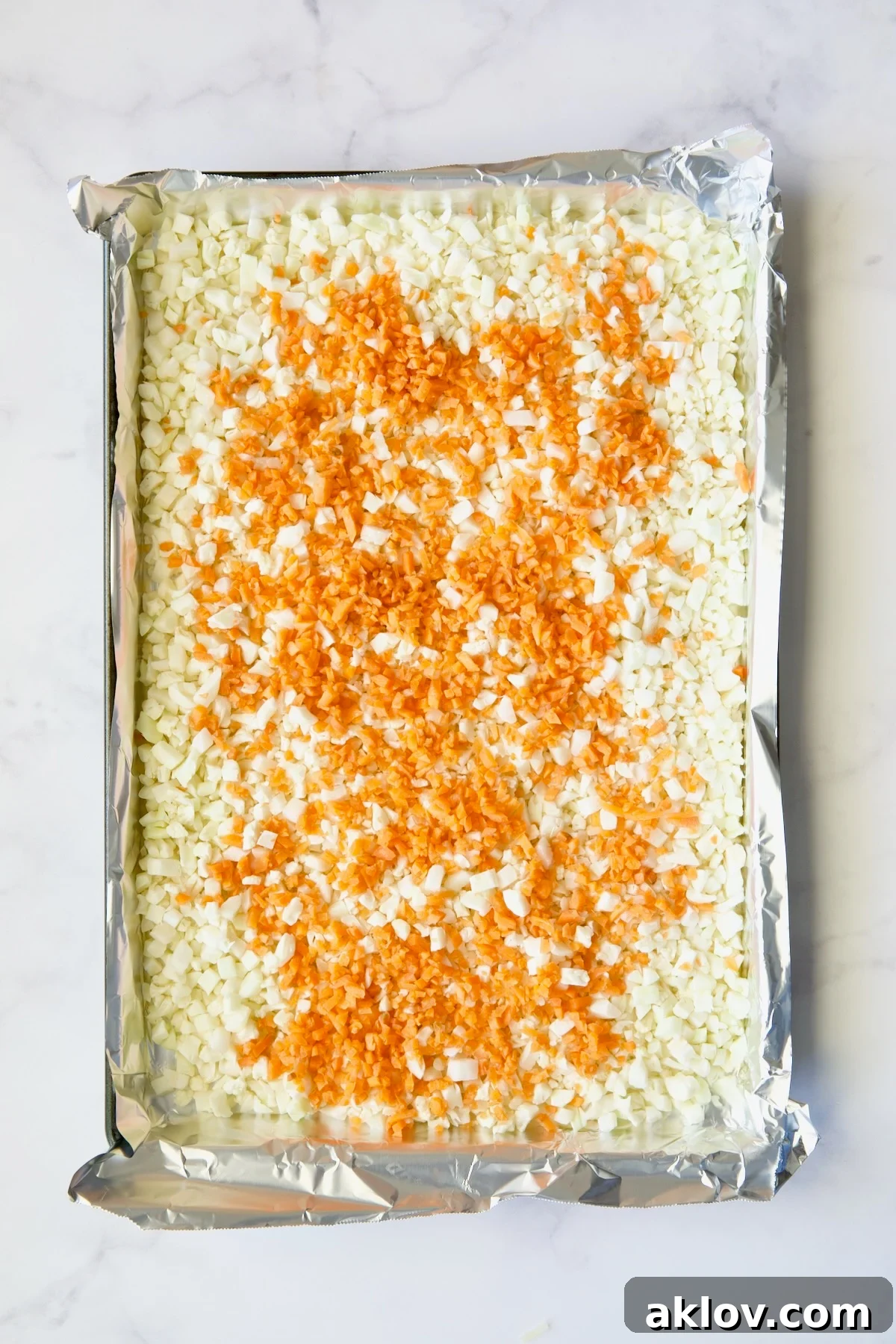 Garlic Parmesan Roasted Riced Veggies 5 Cauliflower rice and diced carrot on aluminum foil-lined baking sheet before being roasted and before being stirred together.
