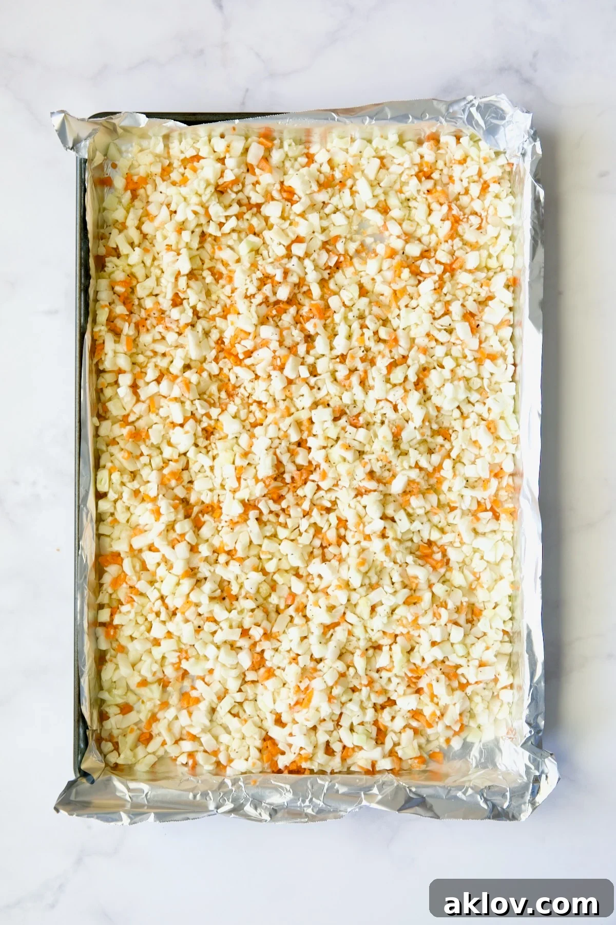 Garlic Parmesan Roasted Riced Veggies 6 Cauliflower rice and diced carrot on aluminum foil-lined baking sheet before being roasted.