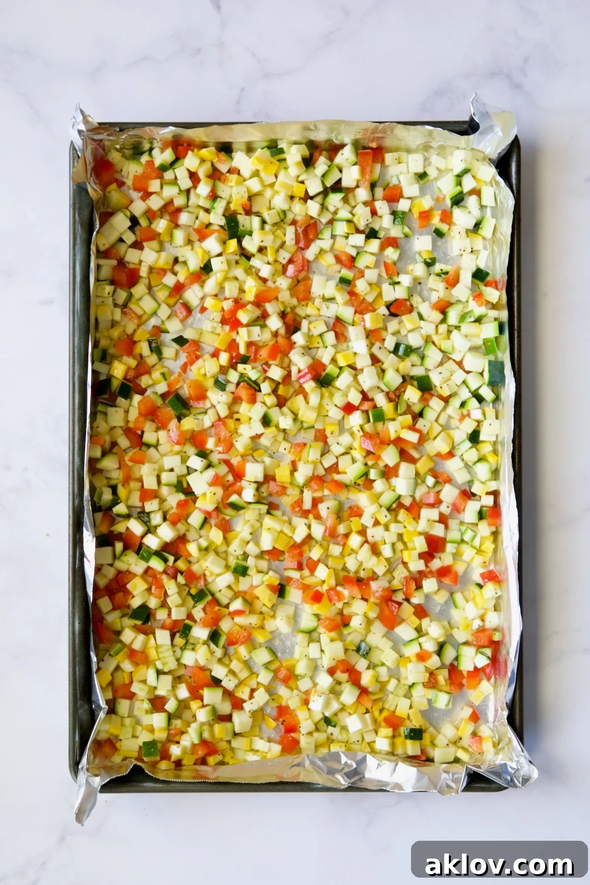 Garlic Parmesan Roasted Riced Veggies 8 Diced zucchini, yellow squash and red bell pepper on aluminum foil-lined baking sheet before being roasted.