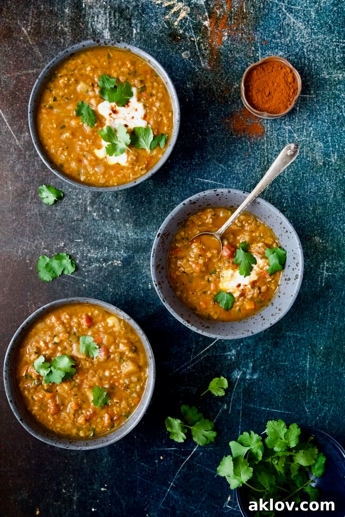 Three beautifully arranged bowls of rich Ethiopian Red Lentil and Vegetable Stew, artfully placed on a rustic blue distressed background, inviting diners to enjoy.