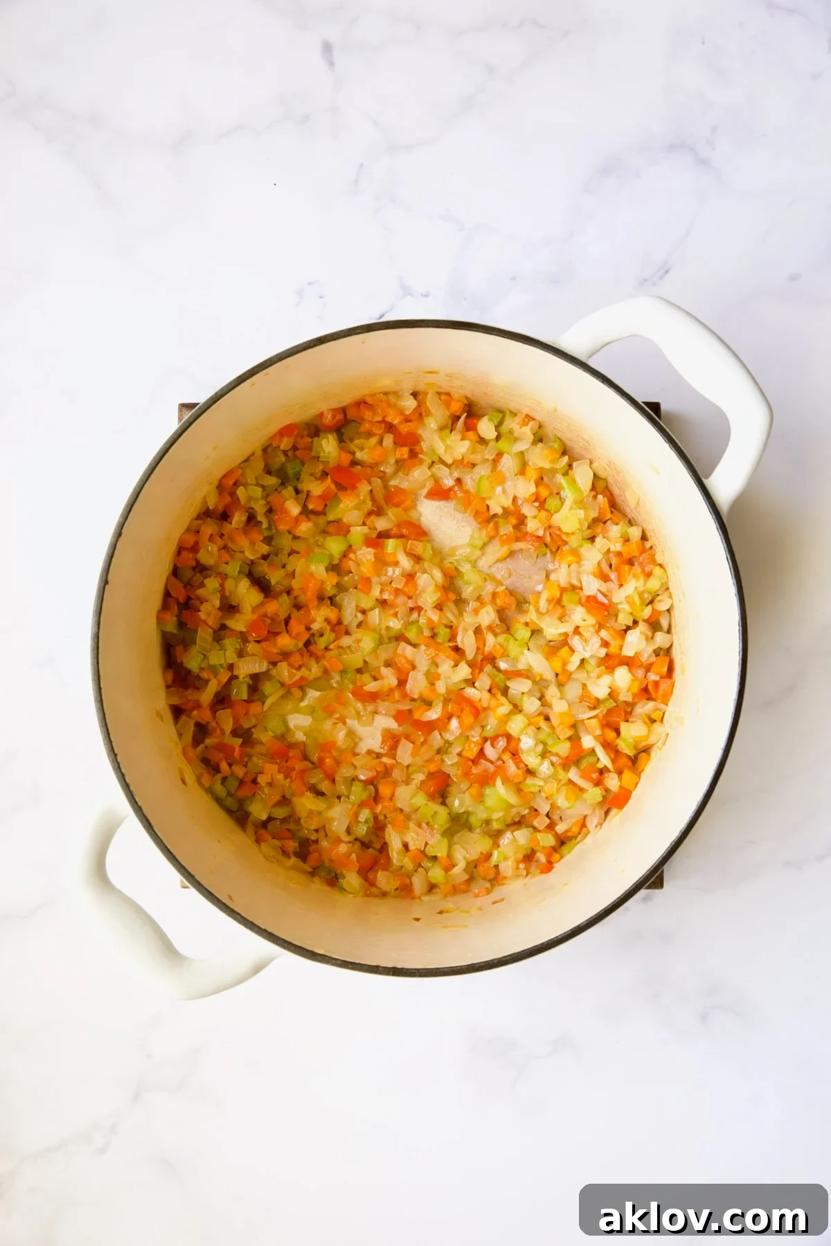 Sautéed onions, vibrant carrots, and crisp celery cooking together in a white Dutch oven, creating a colorful and aromatic vegetable base.