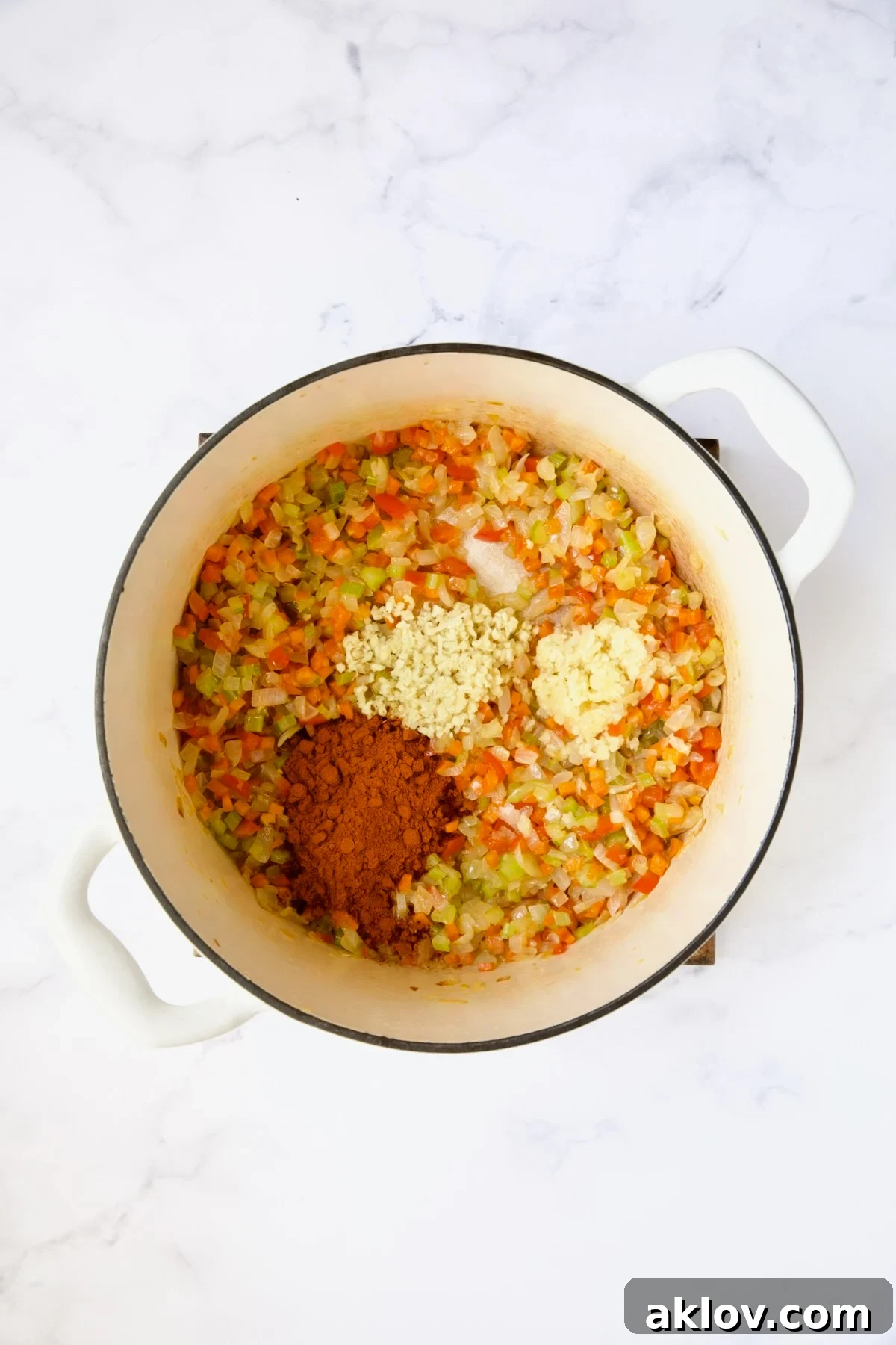A colorful mix of cooked vegetables with minced garlic, ginger, and berbere spice waiting to be stirred in, showcasing distinct ingredients.