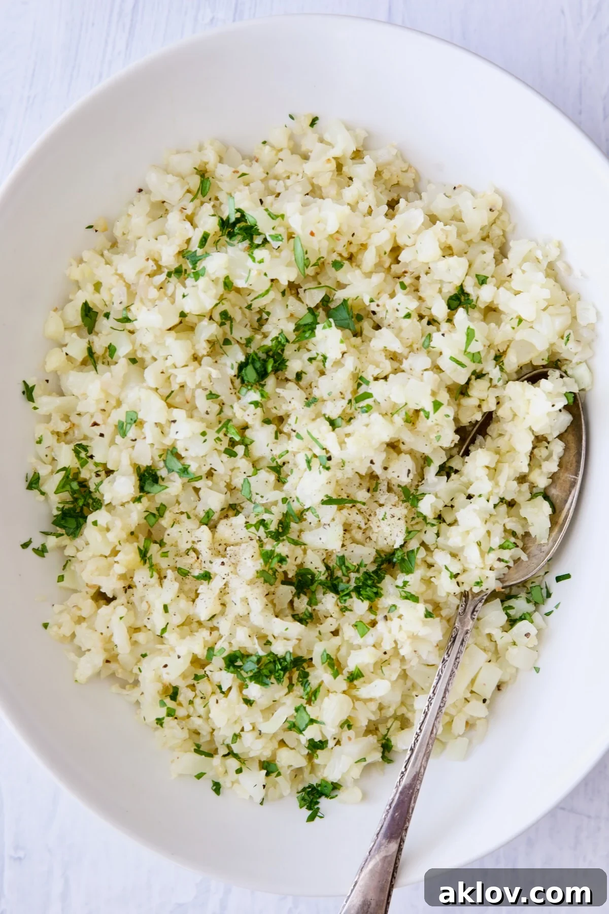 Cauliflower rice garnished with fresh parsley in white oval bowl.