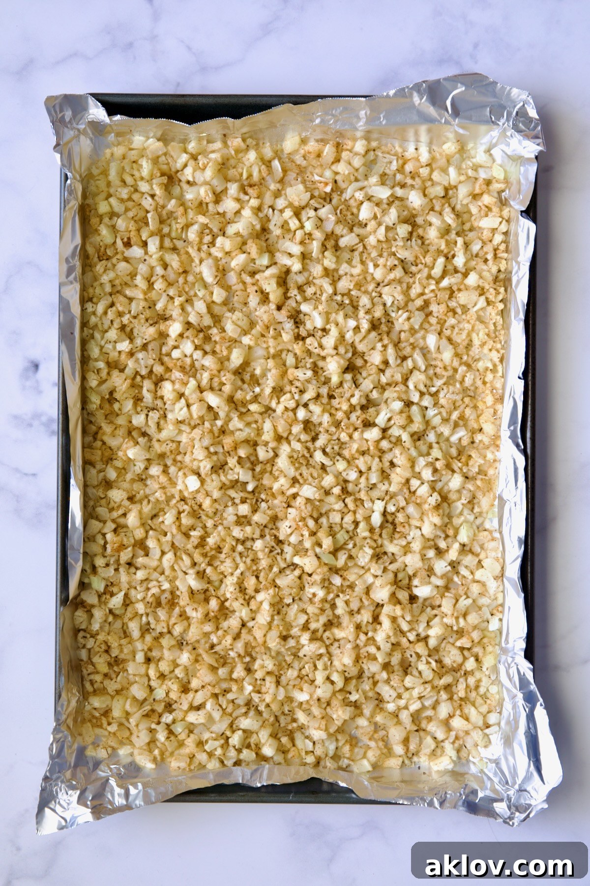 Cooked riced cauliflower on a sheet pan lined with aluminum foil.