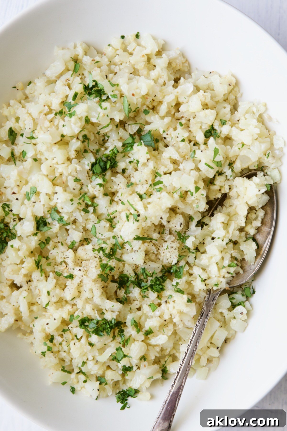 Photo of cauliflower rice in white oval bowl with serving spoon.