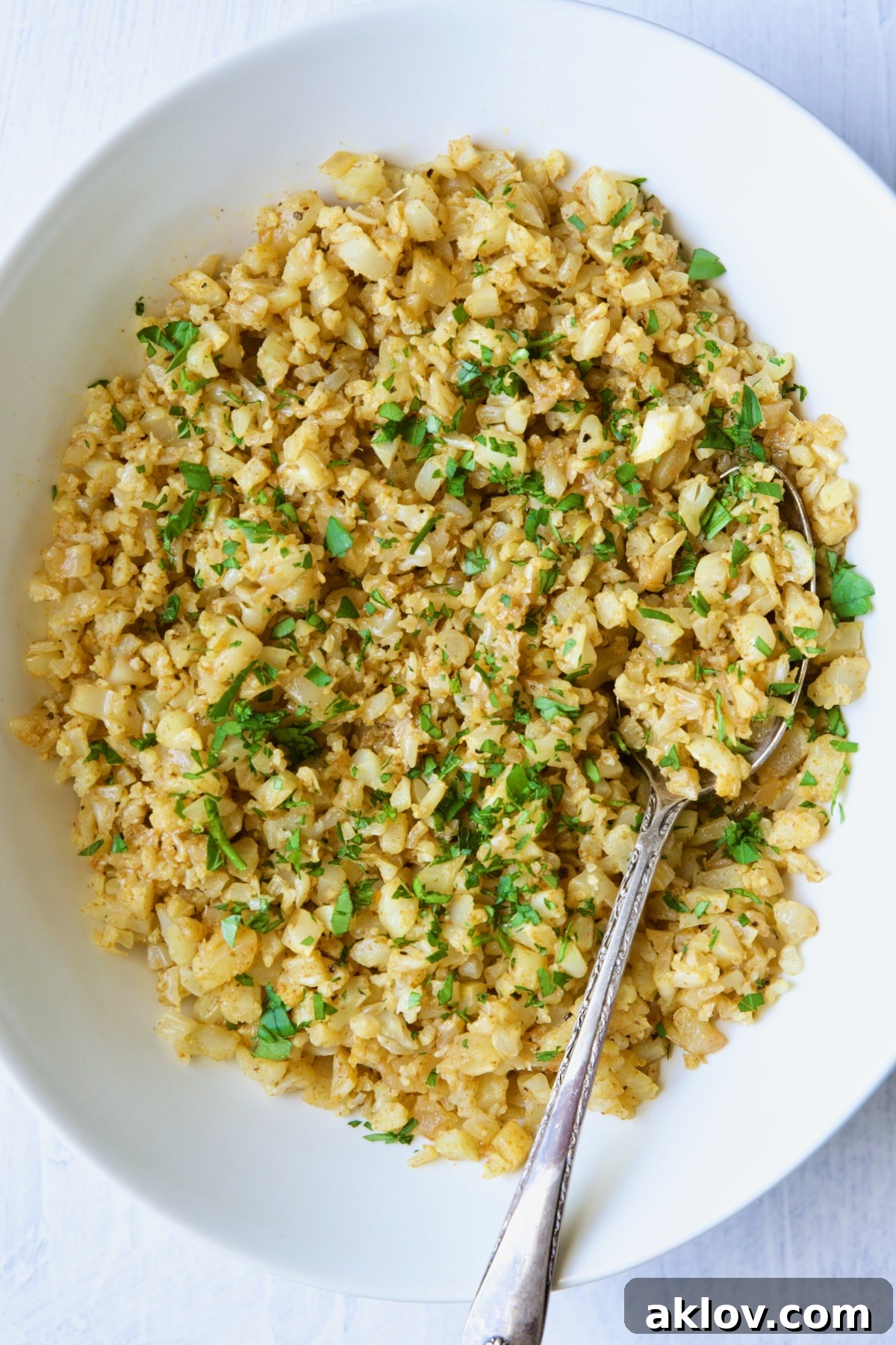 Seasoned cauliflower rice in white oval bowl with serving spoon.