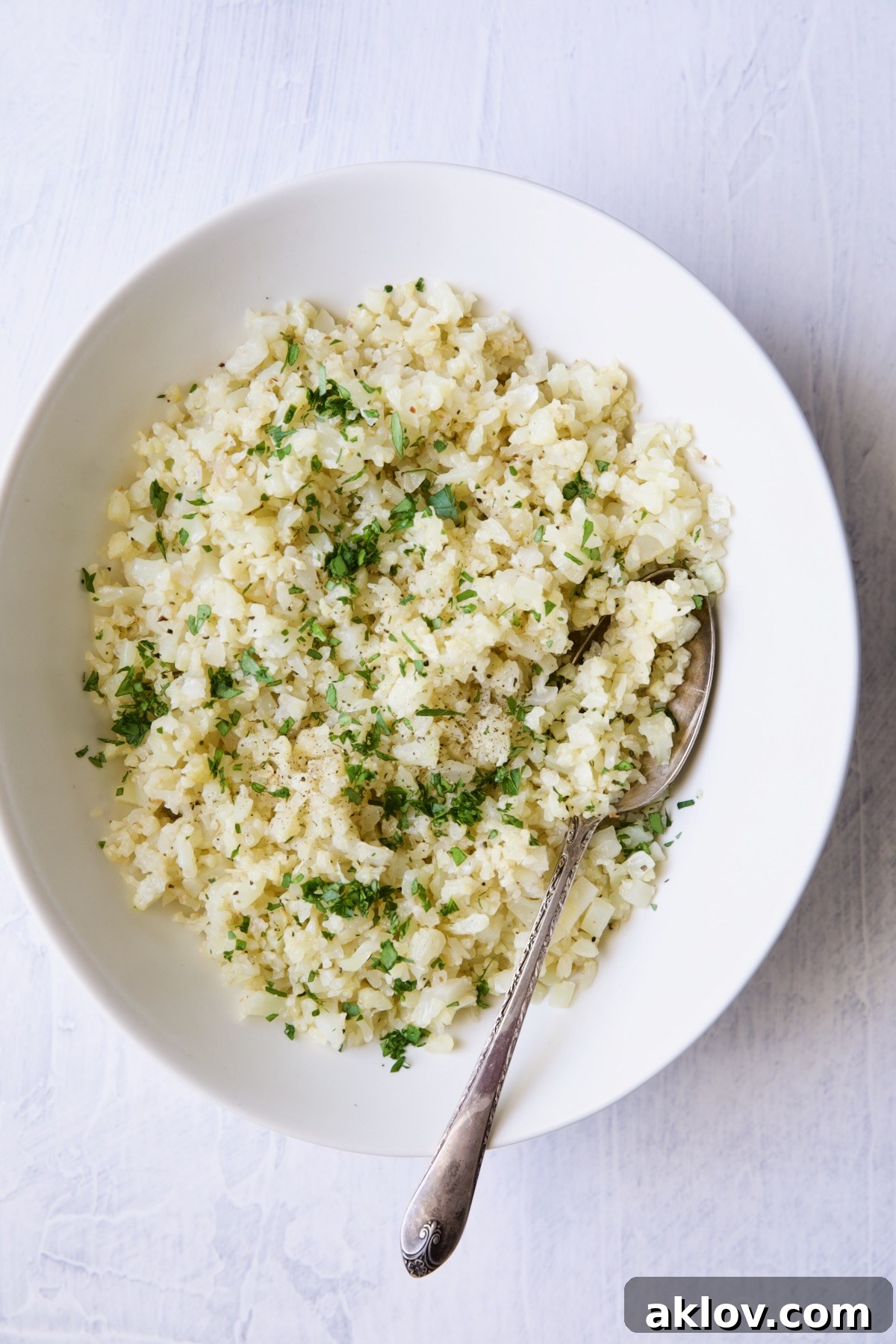 Bowl of plain cauliflower rice in white oval bowl with serving spoon.