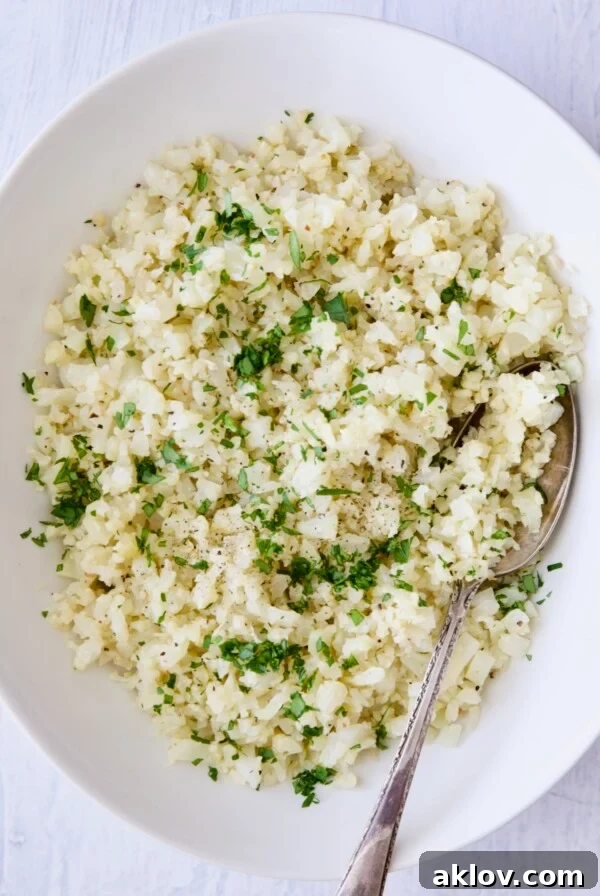 Cauliflower rice garnished with fresh parsley in white oval bowl.