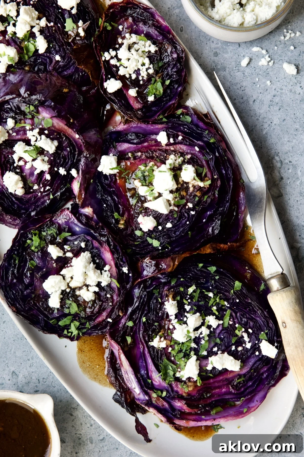 Roasted Red Cabbage Steaks with Balsamic Vinaigrette and Goat Cheese on white platter with serving fork.