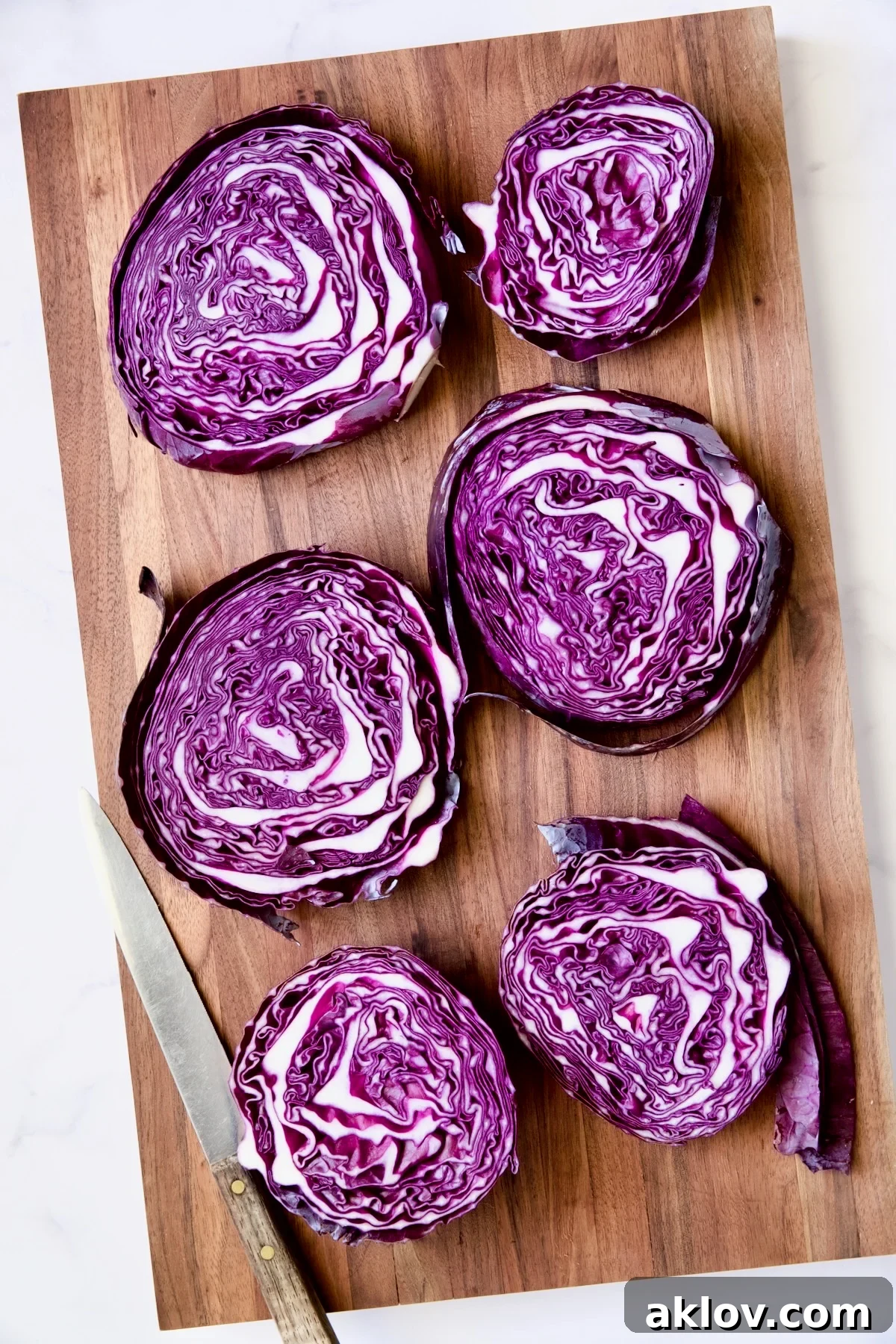 Six red cabbage slices on wood cutting board.