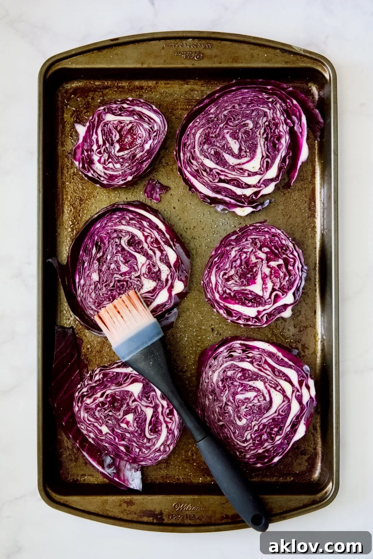 Red cabbage wedges on baking sheet being brushed with olive oi.
