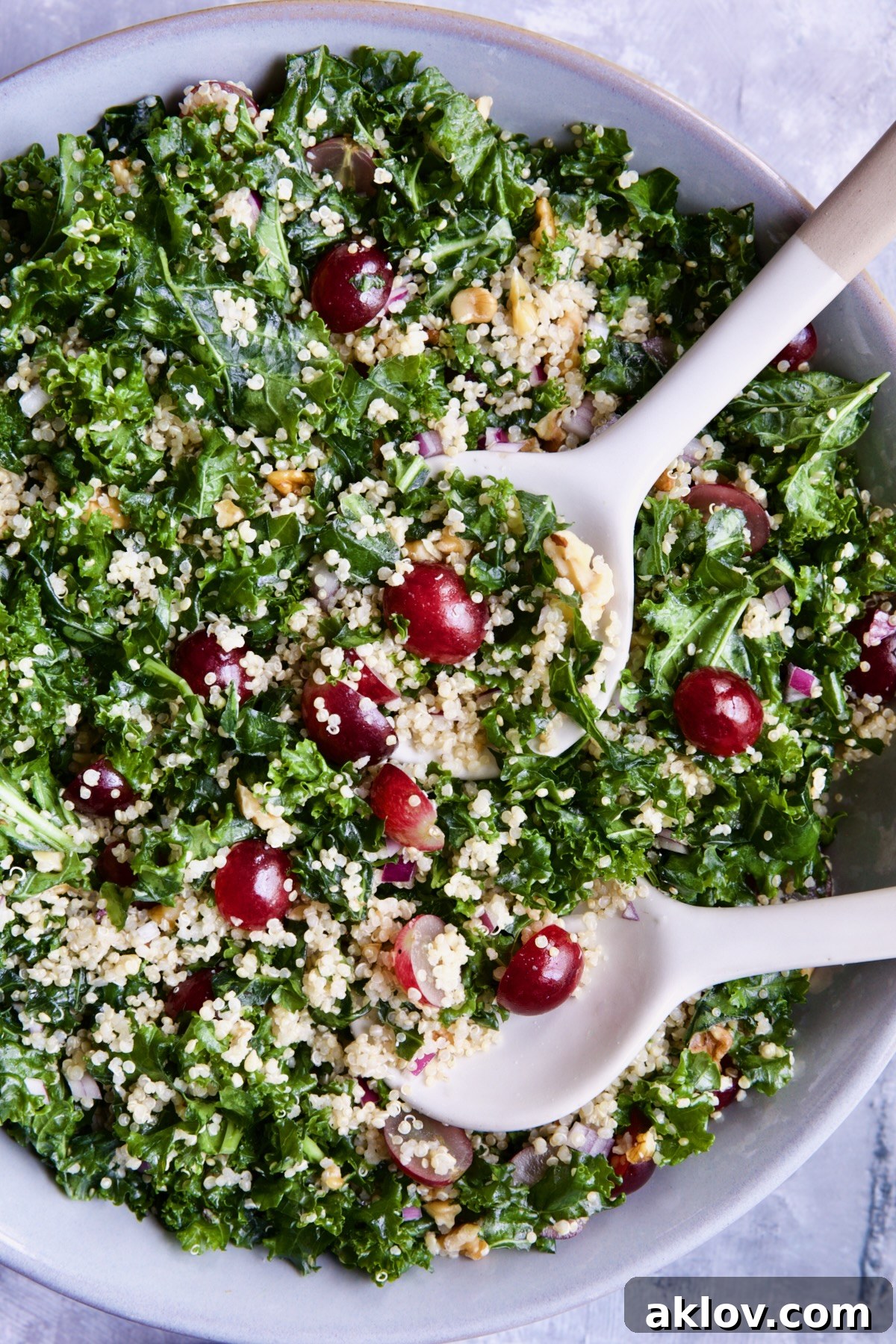 Another enticing view of the Kale Quinoa Salad with Lemon Honey Dressing, presented in a stylish gray serving bowl with accompanying serving utensils.