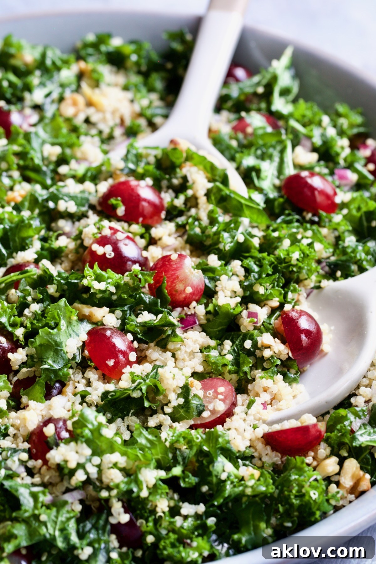 Serving utensils scooping up a generous portion of the fresh Kale Quinoa Salad with Lemon Honey Dressing from a bowl.