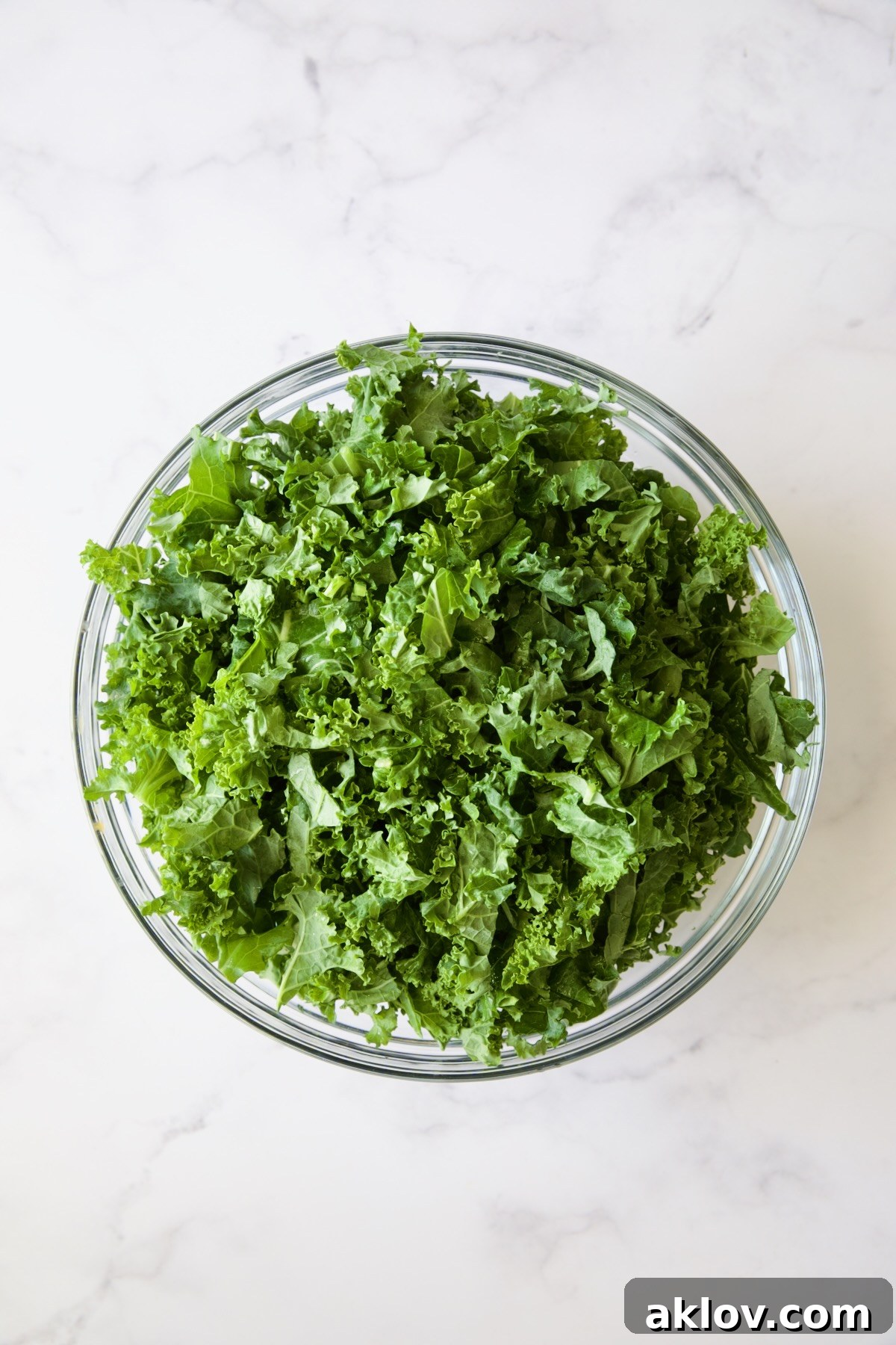 Fresh, raw kale leaves in a glass bowl before being massaged.