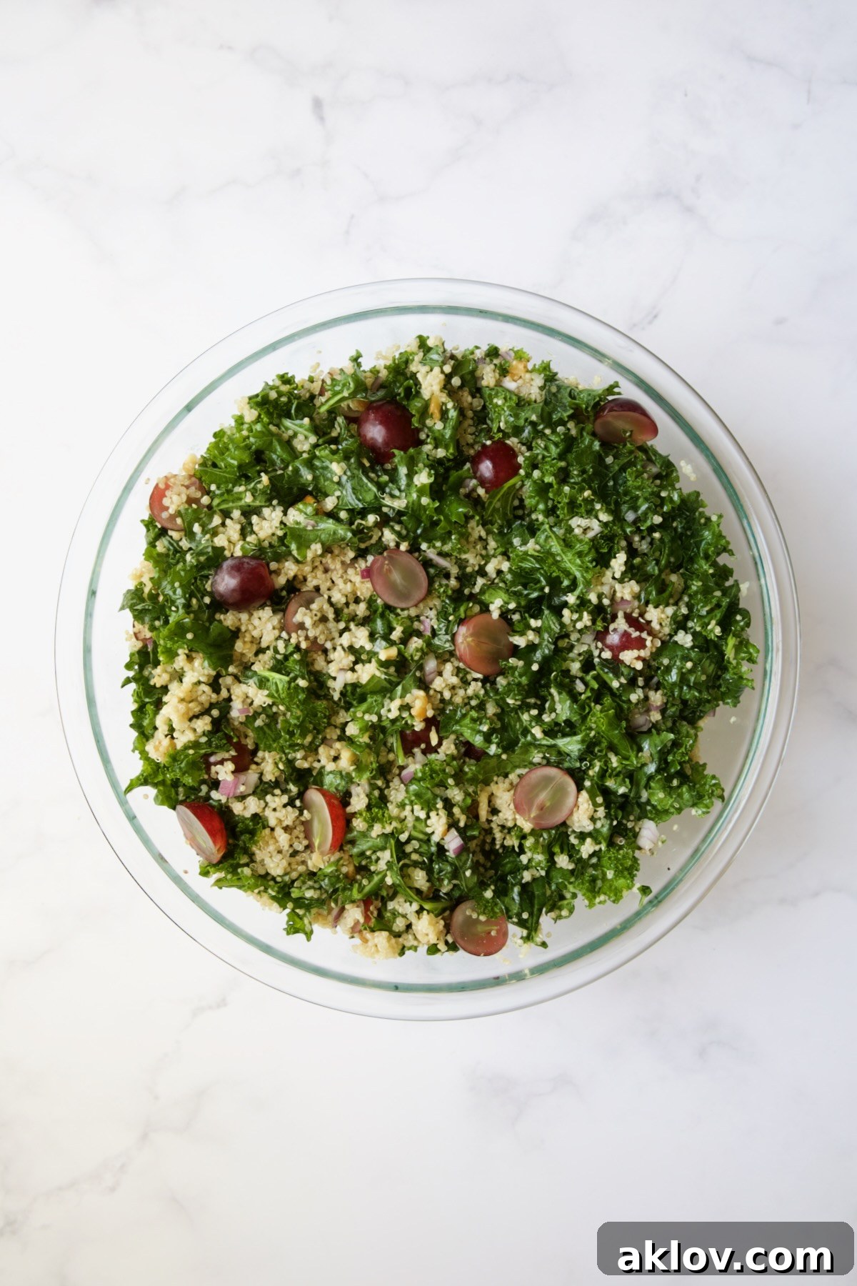 The same ingredients – kale, quinoa, walnuts, red grapes, and red onion – now beautifully mixed and combined in a glass bowl.