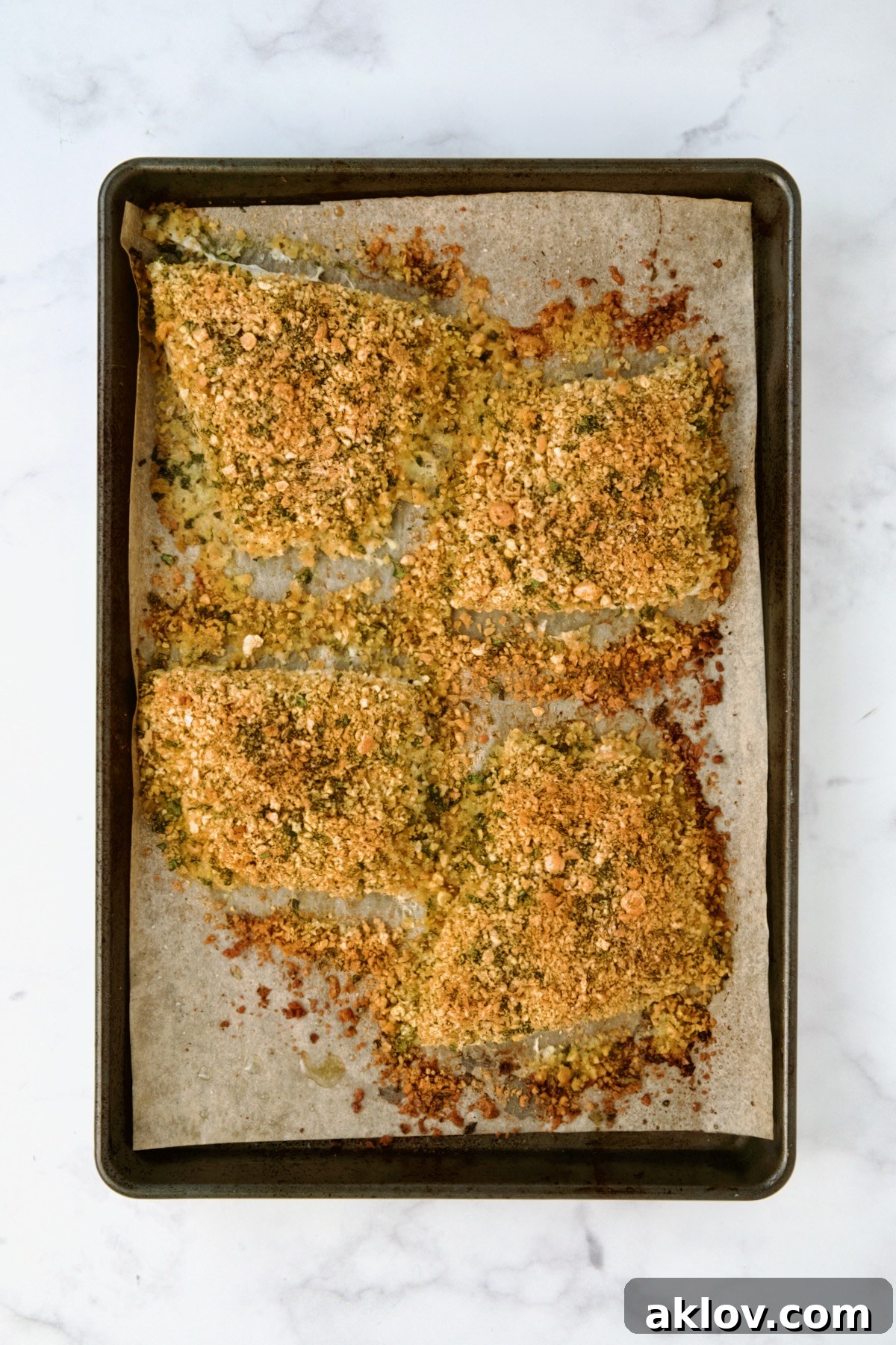Crispy Chickpea-Crusted Fish with Zesty Jalapeno Tartar 11 Four golden-brown, crispy chickpea-crusted fish fillets baked on a parchment paper-lined baking sheet, just out of the oven.