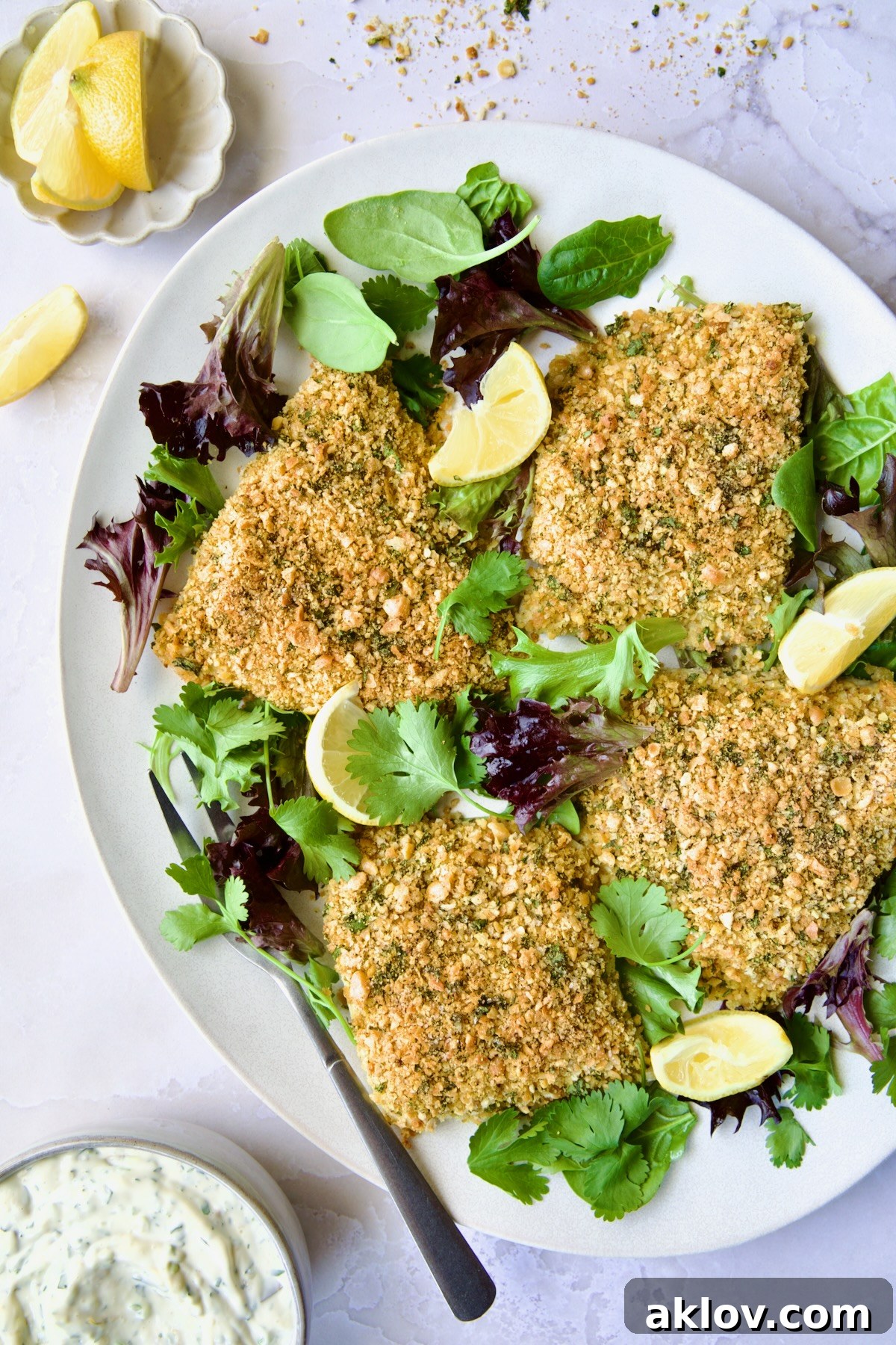 Crispy Chickpea-Crusted Fish with Zesty Jalapeno Tartar 12 Crispy Chickpea-Crusted Fish displayed on an oval white platter, adorned with fresh baby greens and a serving fork, ready for plating.