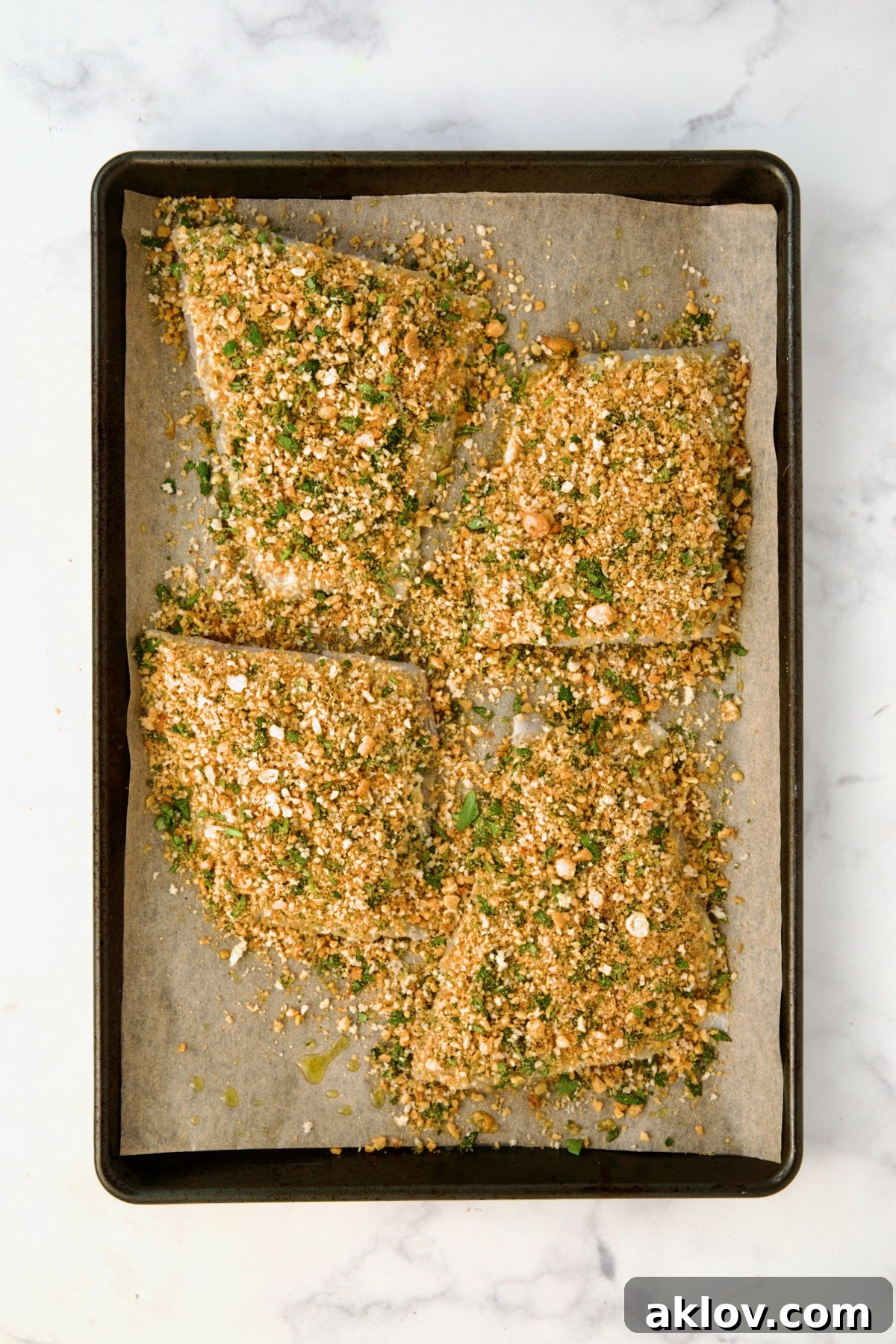 Crispy Chickpea-Crusted Fish with Zesty Jalapeno Tartar 10 Four pieces of white fish fillets on a baking sheet are uniformly topped with the crispy chickpea mixture, ready for baking.