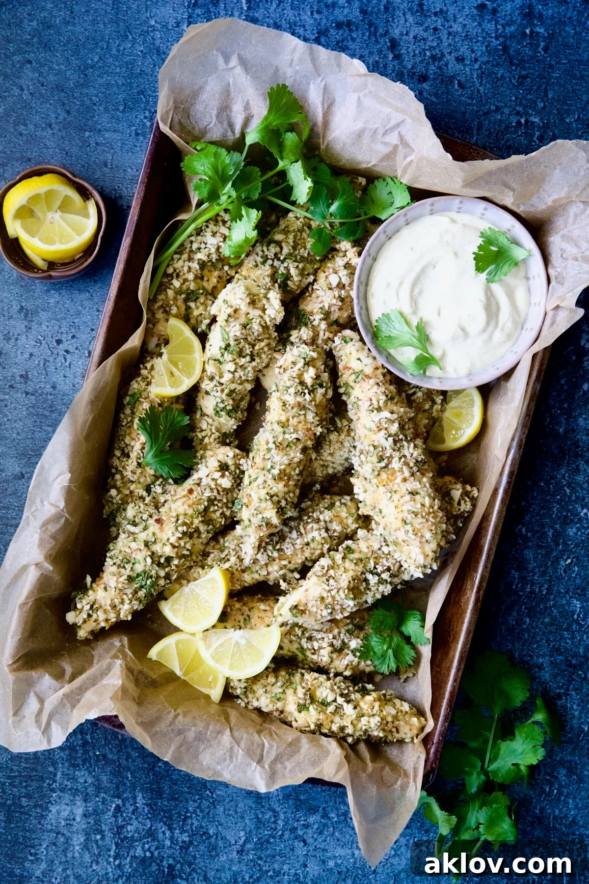 Almond-Crusted Chicken Tenders with Lemon Curry Mayonnaise in parchment paper-lined pan garnished with lemon wedges and cilantro.