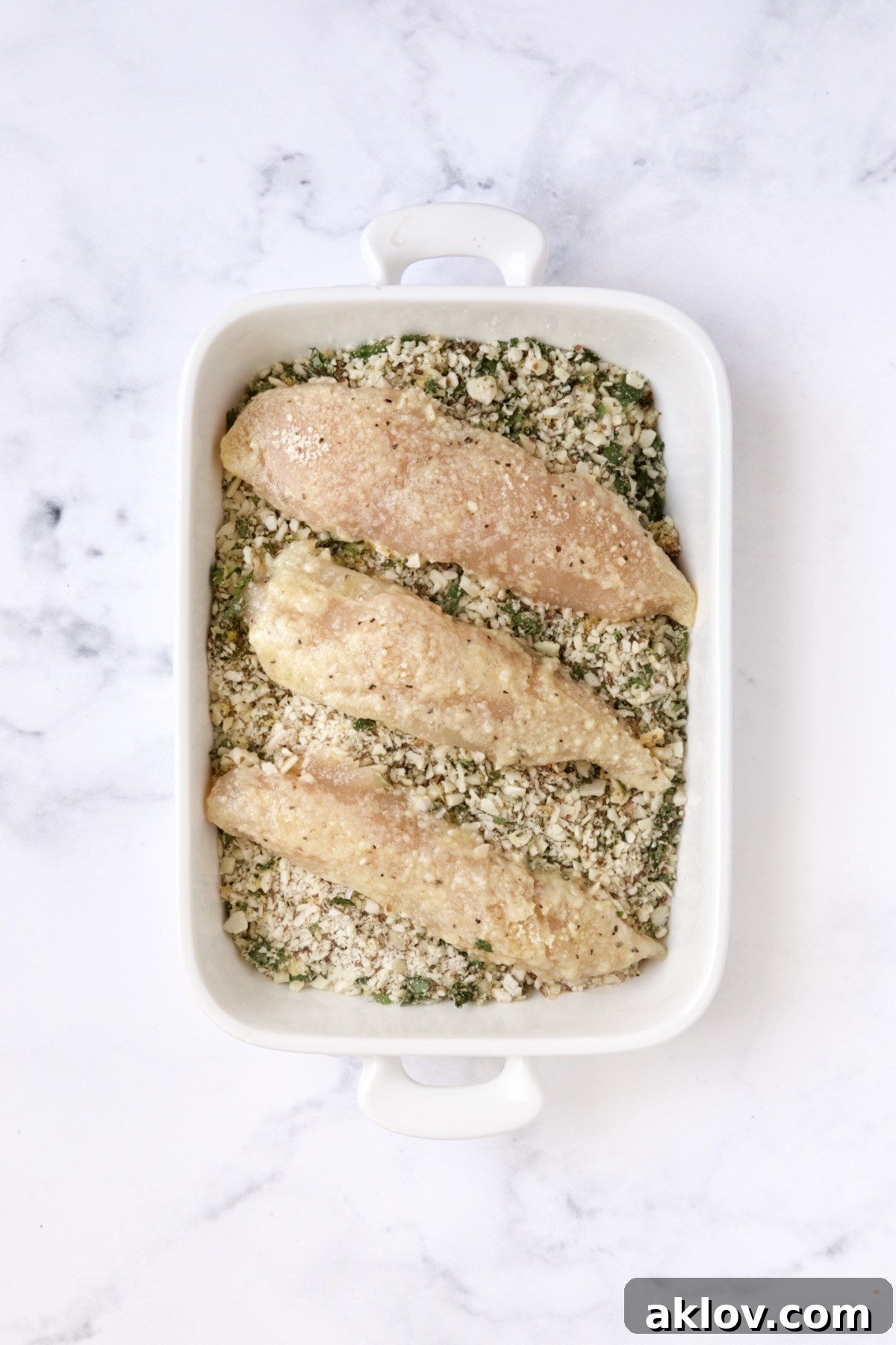 Three chicken tenders in almond coating in white rectangular baking pan.
