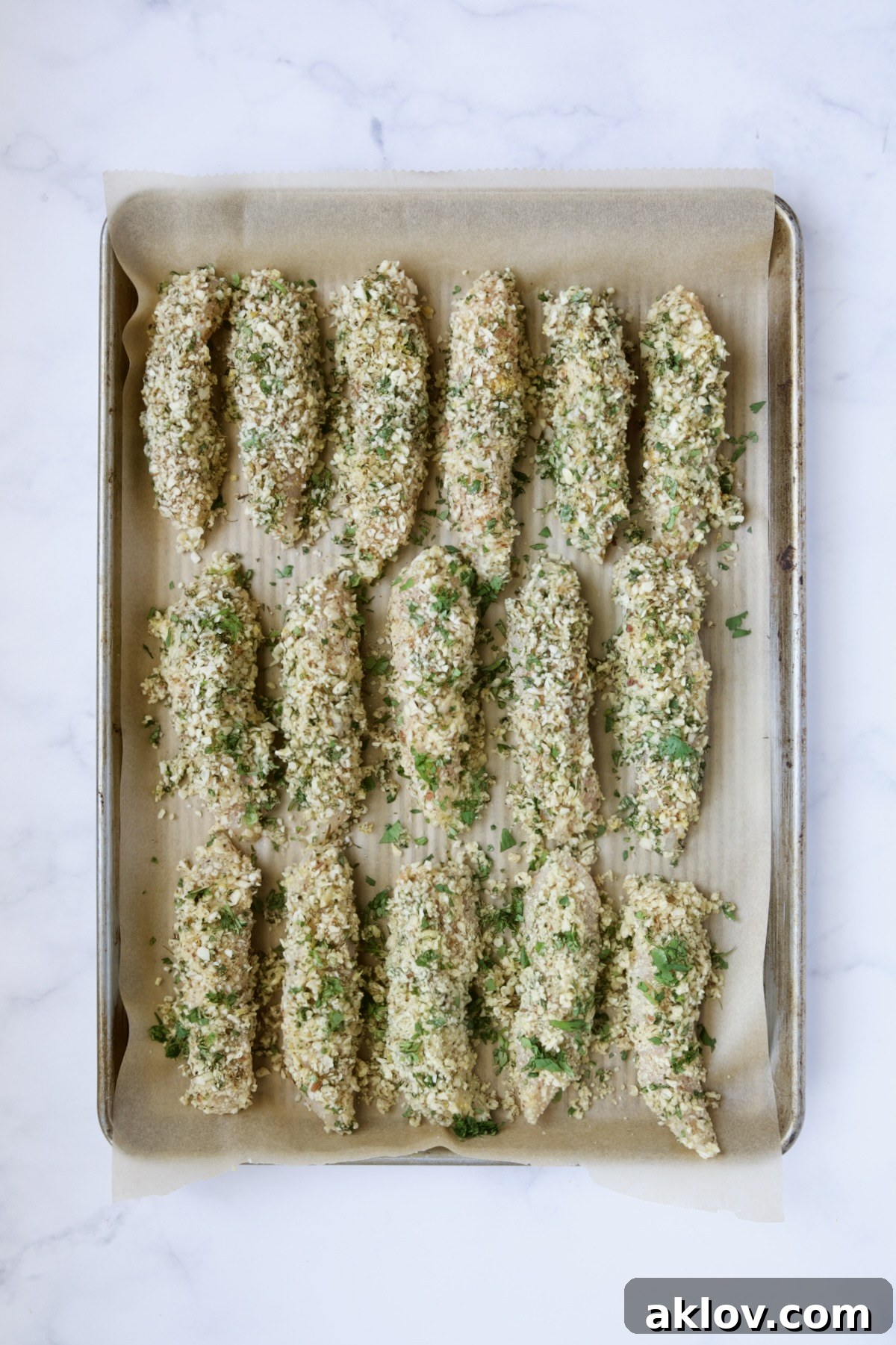 Almond coated chicken tenders on parchment paper-lined rimmed baking sheet.