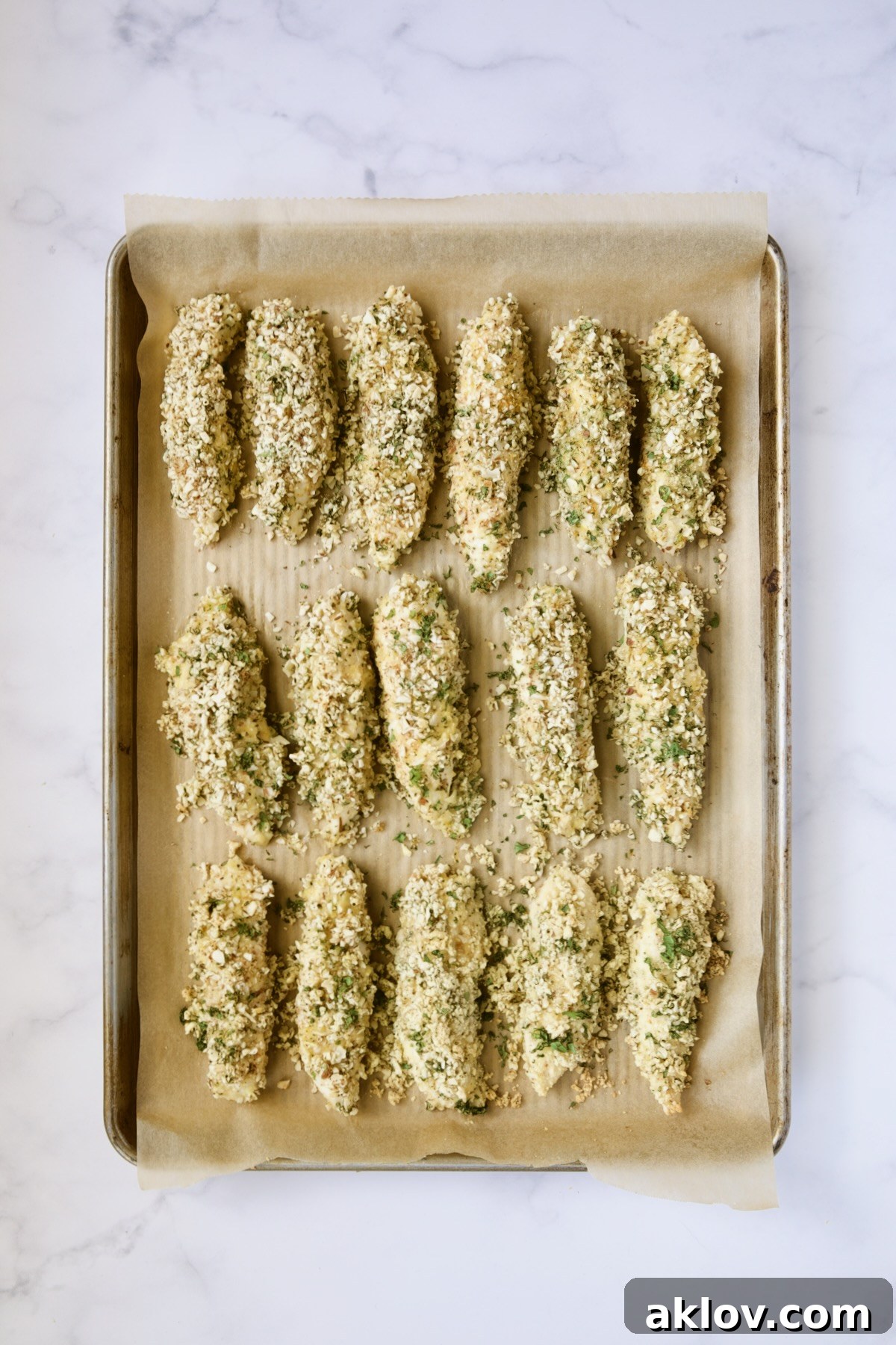 Baked almond coated chicken tenders on parchment paper-lined rimmed baking sheet.