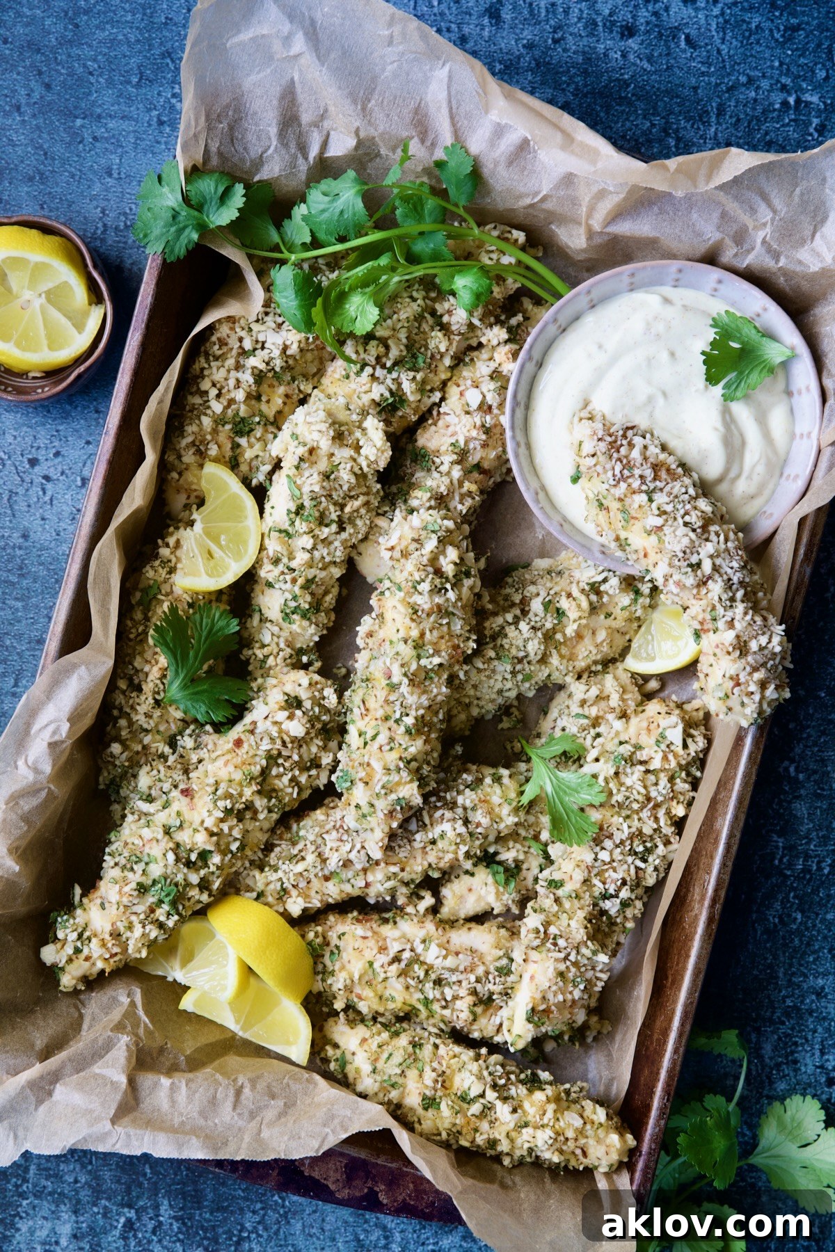 Almond-Crusted Chicken Tenders with Lemon Curry Mayonnaise with one tender dipped into mayonnaise garnished with lemon and cilantro.