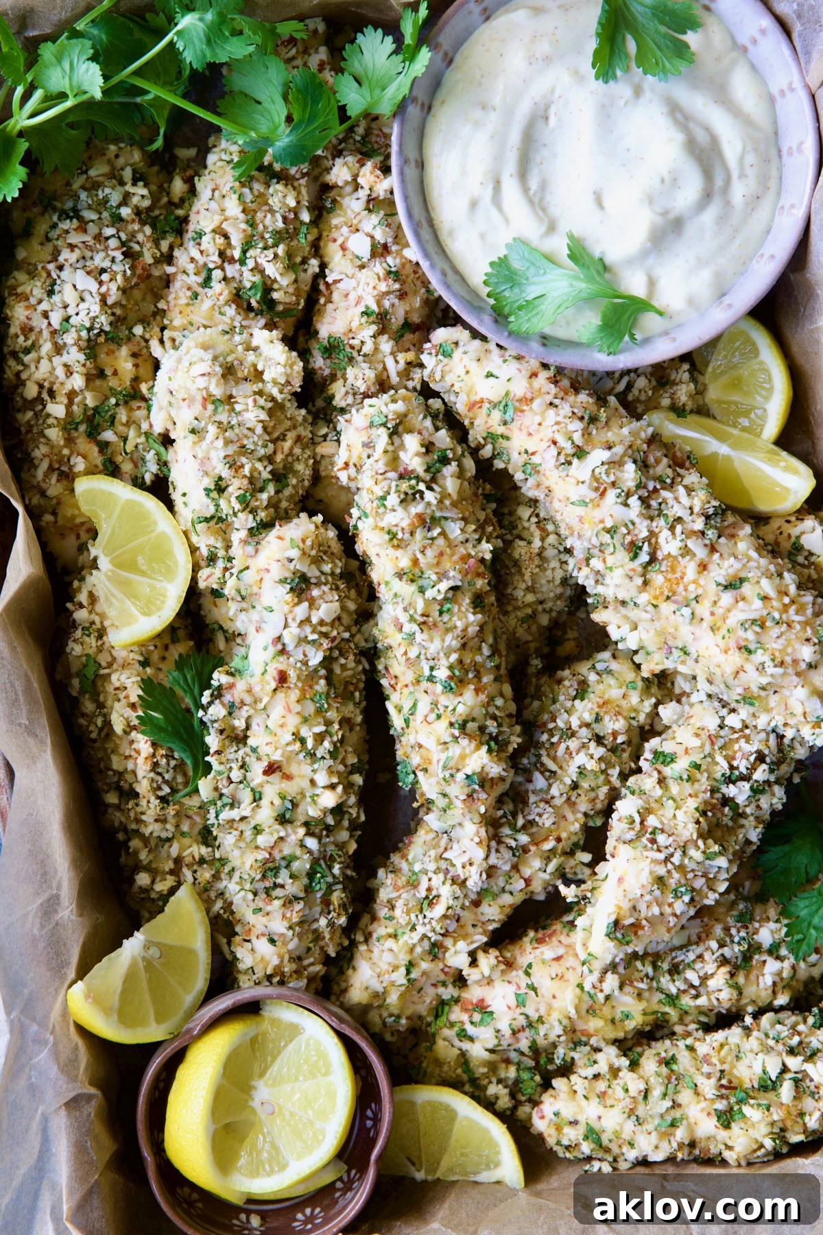 Almond-Crusted Chicken Tenders with Lemon Curry Mayonnaise with cilantro sprigs and lemon wedges.