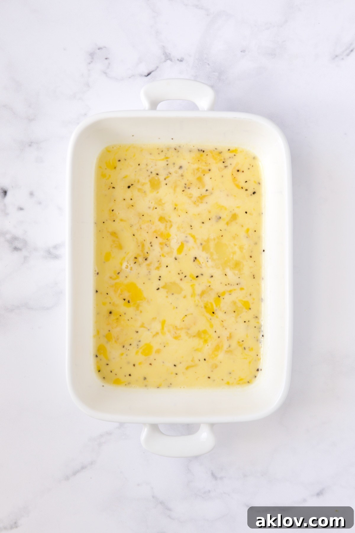 Seasoned beaten eggs in white rectangular pan.