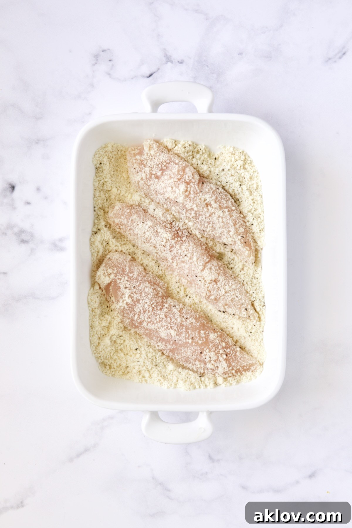 Three chicken tenders in almond flour in white rectangular baking pan.