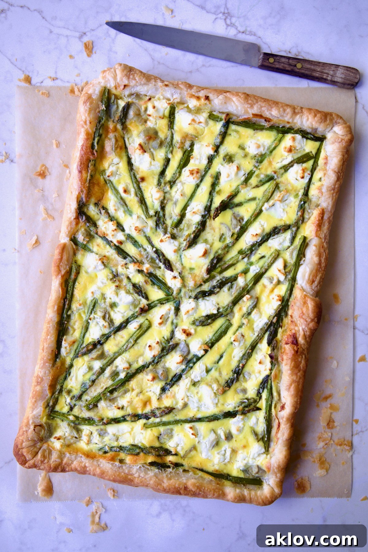 Whole Puff Pastry Vegetable Tart on brown parchment paper with knife nearby.