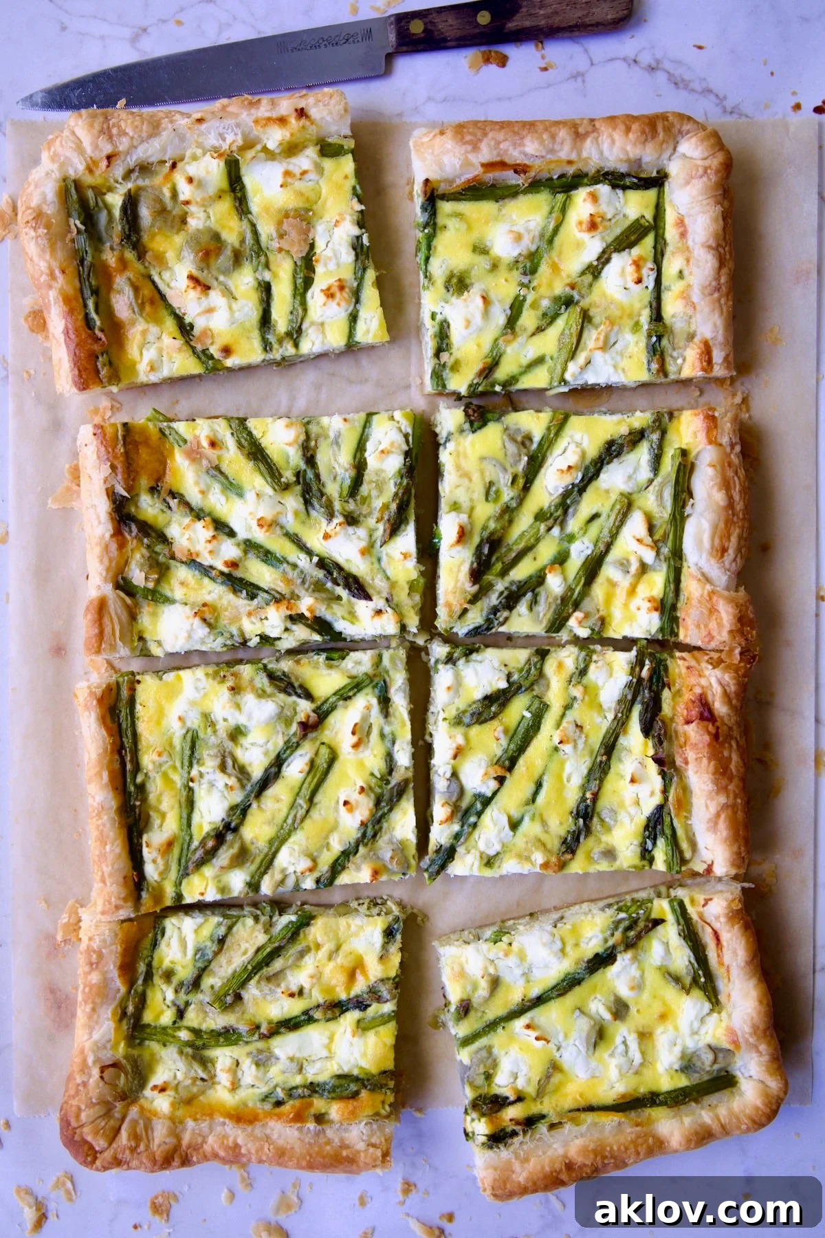 Eight pieces of Puff Pastry Vegetable Tart on brown parchment paper with knife nearby.