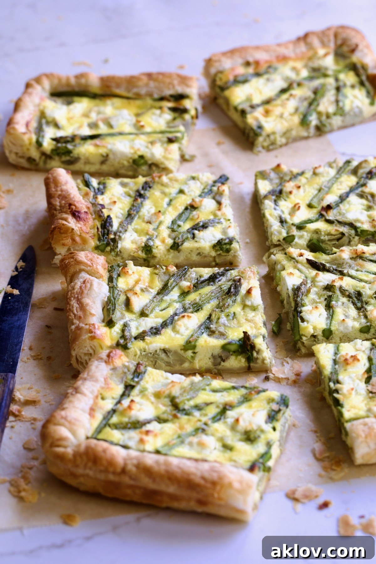 Eight pieces of Puff Pastry Vegetable Tart on brown parchment paper with knife nearby.