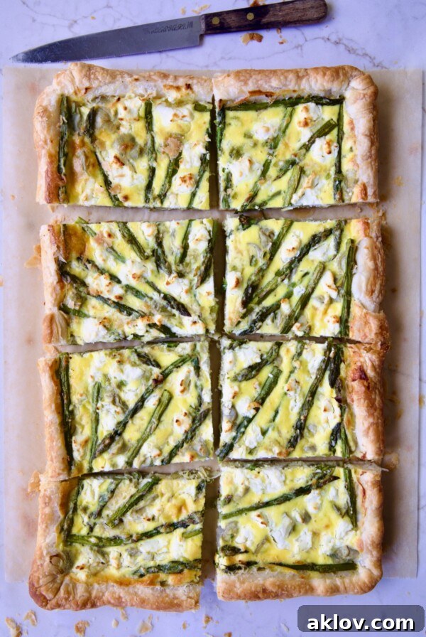 Puff Pastry Vegetable Tart on brown parchment paper cut into eight pieces with knife nearby.