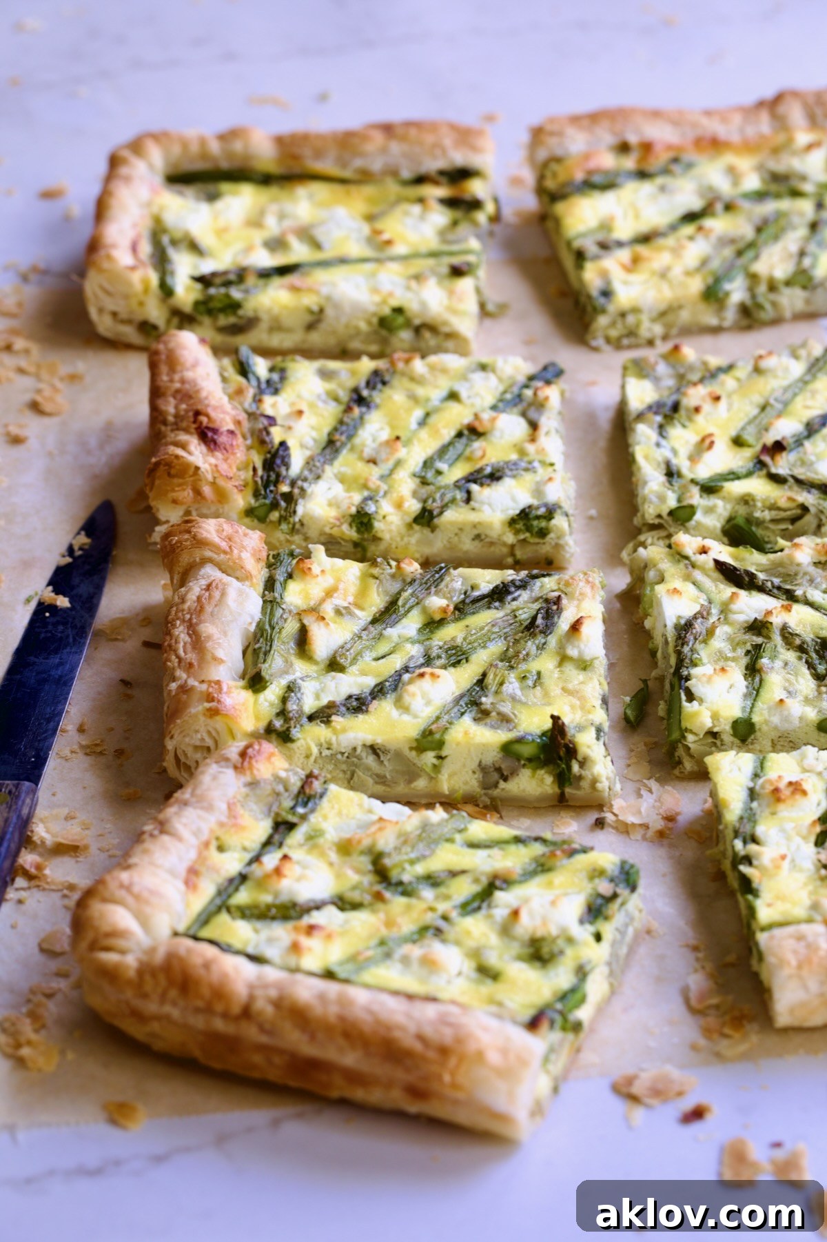 Eight pieces of Puff Pastry Vegetable Tart on brown parchment paper with knife nearby.