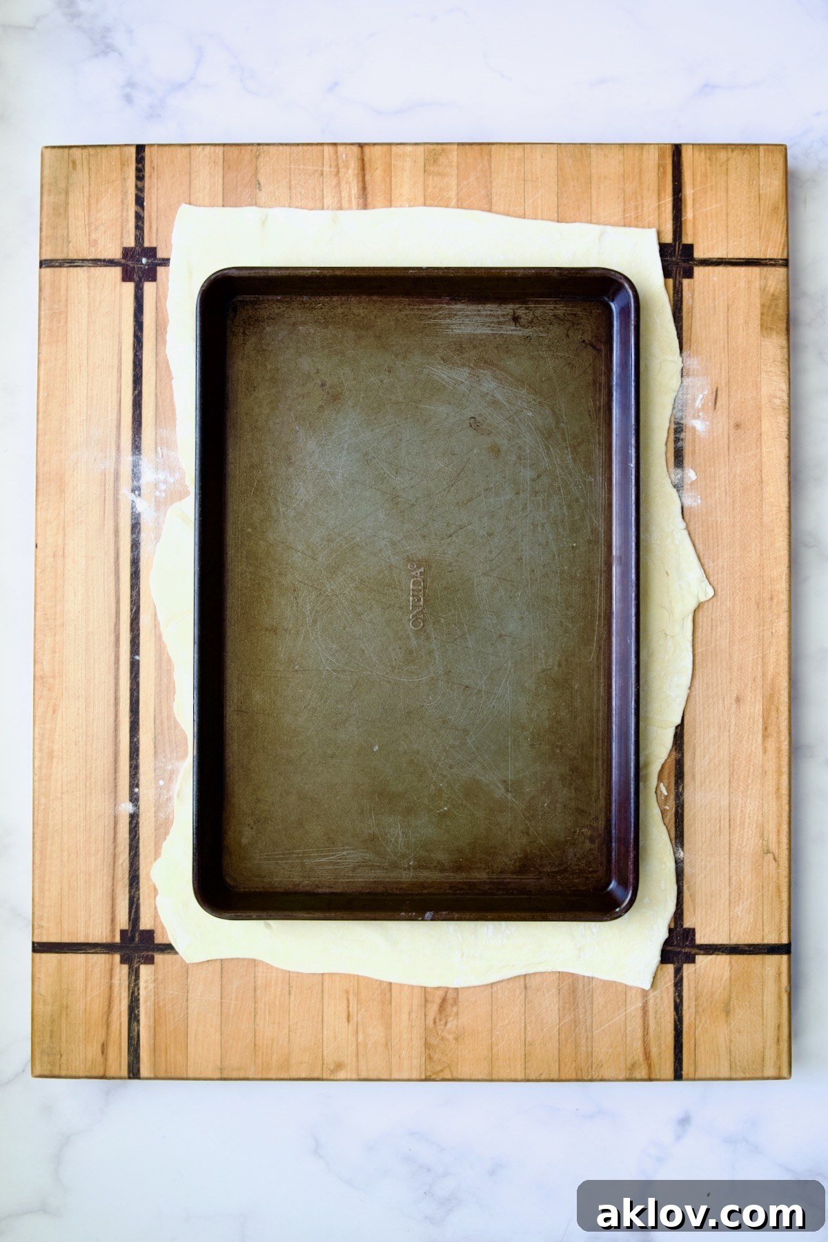Sheet pan set over puff pastry crust on wood cutting board.