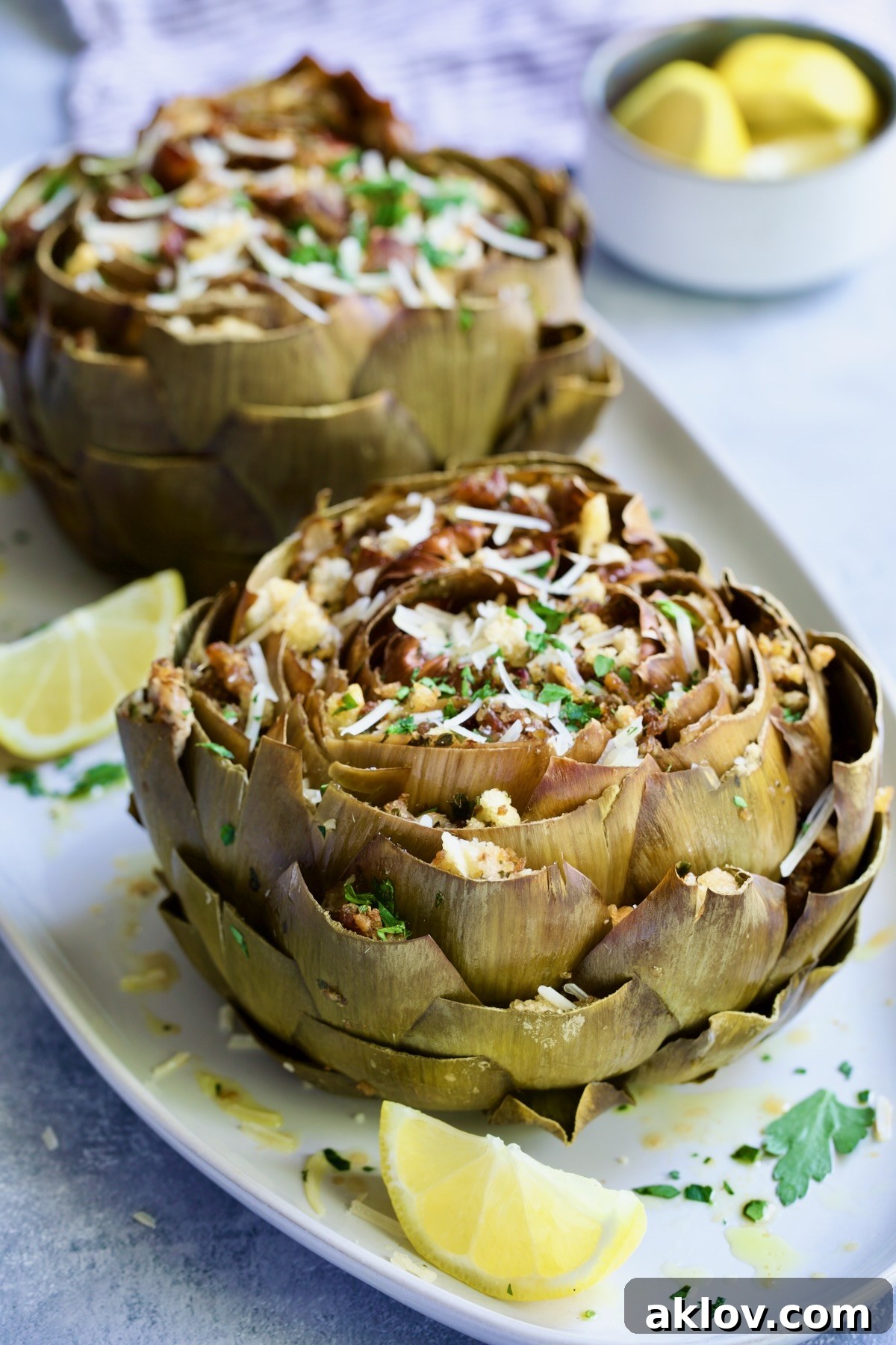 Savory Italian Stuffed Artichokes 16 Two Italian-Stuffed Artichokes on white plates with lemon wedges.