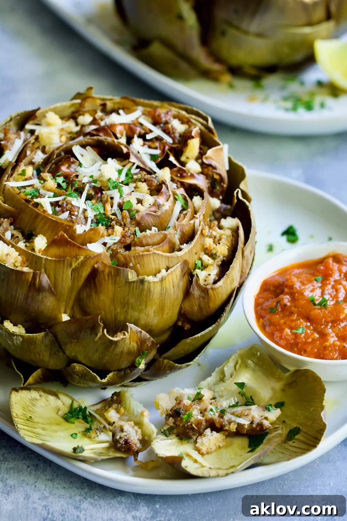 Savory Italian Stuffed Artichokes 18 Stuffed artichoke on white plate with marinara sauce.