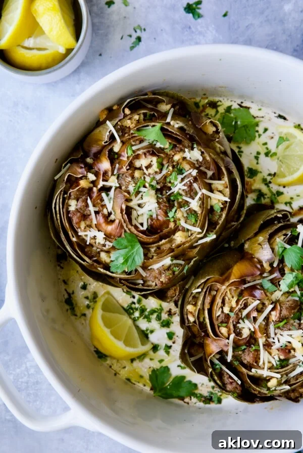 Baked Italian-Stuffed Artichokes in white baking dish garnished with lemon wedges.