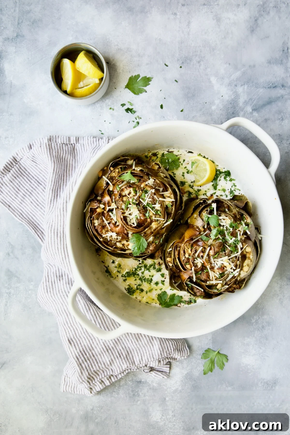 Savory Italian Stuffed Artichokes 3 Two Italian-Stuffed Artichokes in white baking dish with lemon wedges and parsley.
