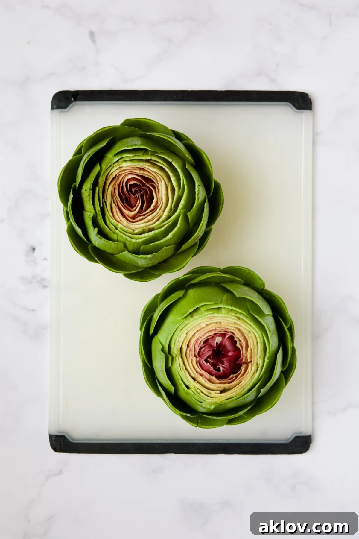 Savory Italian Stuffed Artichokes 10 Two trimmed artichokes on white cutting board.
