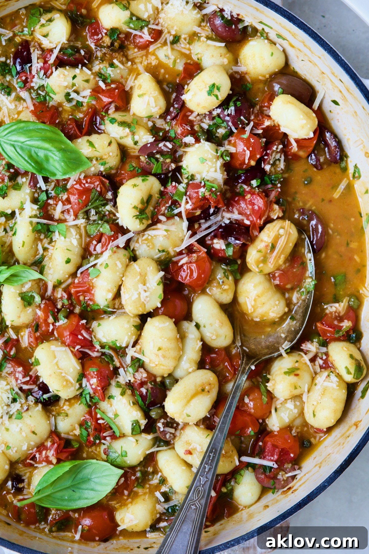 Gnocchi with Cherry Tomato Puttanesca Sauce with some on serving spoon in white enamel cast iron skillet.