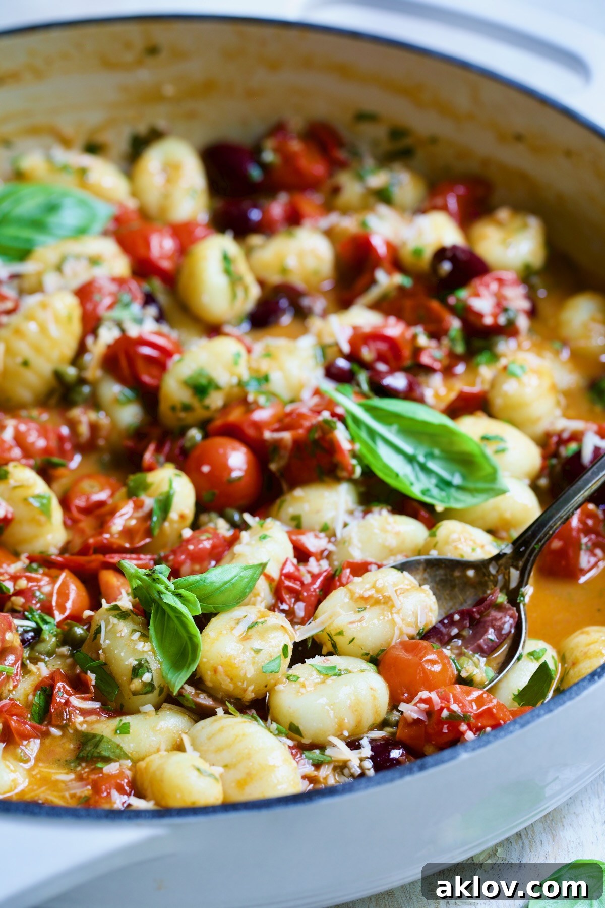 Gnocchi with Cherry Tomato Puttanesca Sauce in white enamel cast iron skillet with serving spoon scooping some up.